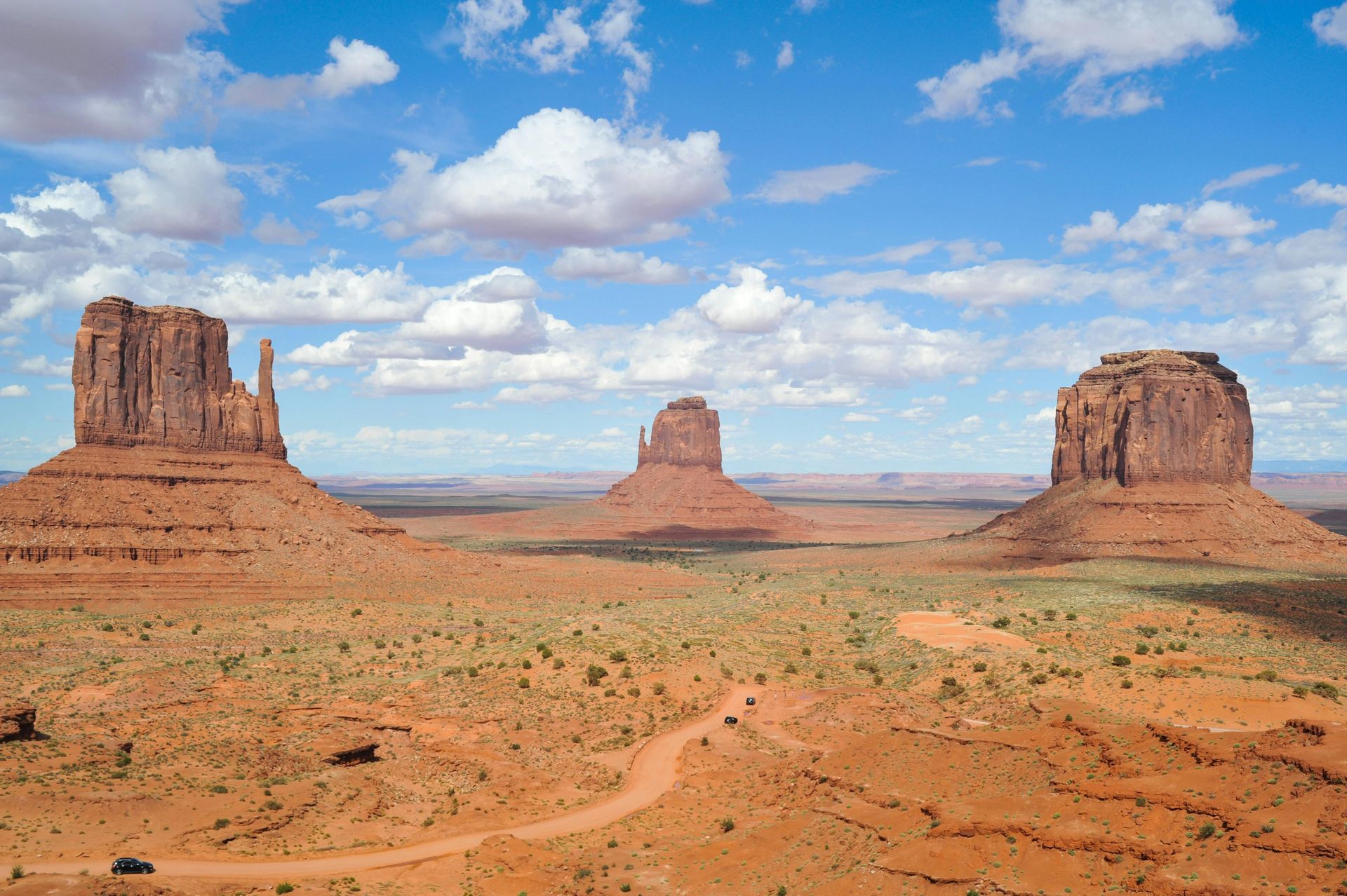 Monument Valley landscape with three sandstone buttes under a blue sky with clouds.