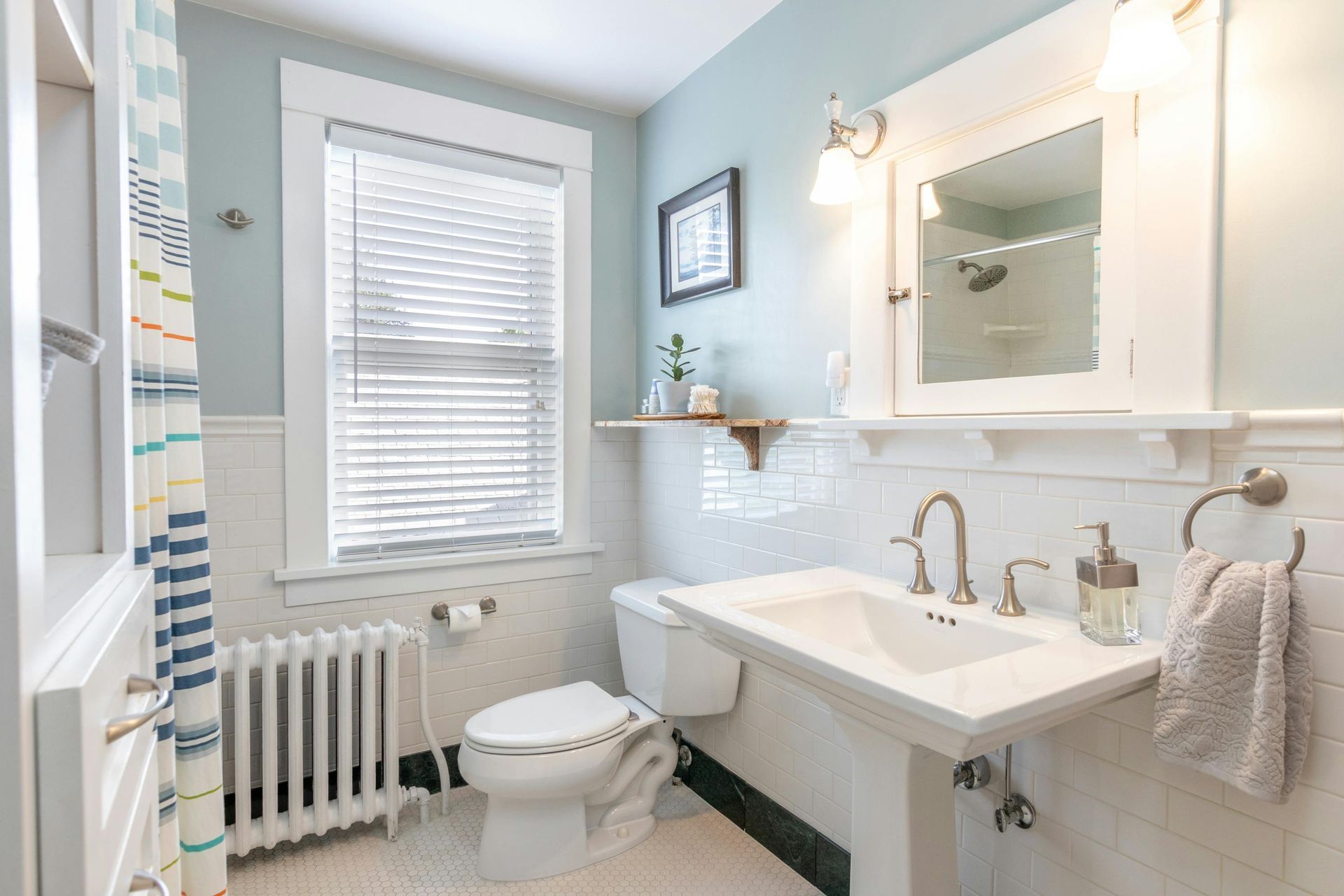 Small, light blue bathroom with white fixtures and window blinds.