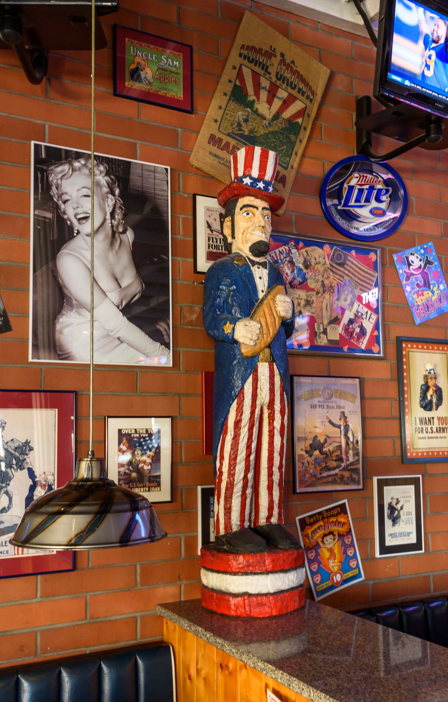 Brick-wall diner display with Uncle Sam statue, Marilyn poster, and framed retro signs