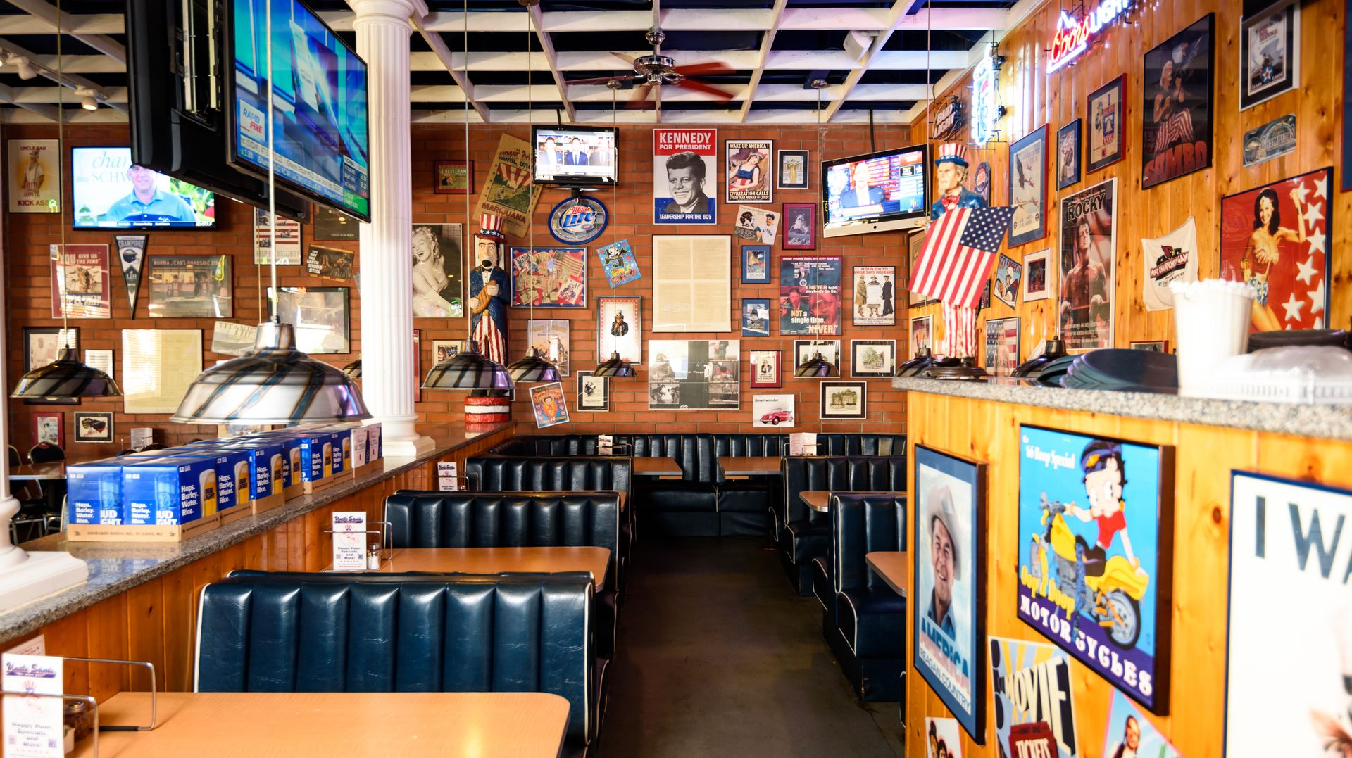 Empty diner booth with blue seating, wooden tables, and walls covered in framed photos and posters.