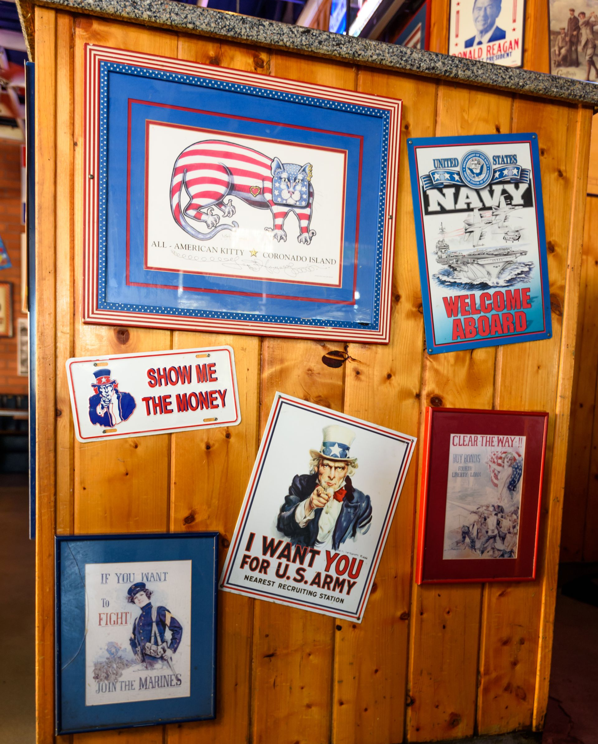 Wooden wall with framed patriotic signs and vintage-style posters in red, blue, and white.
