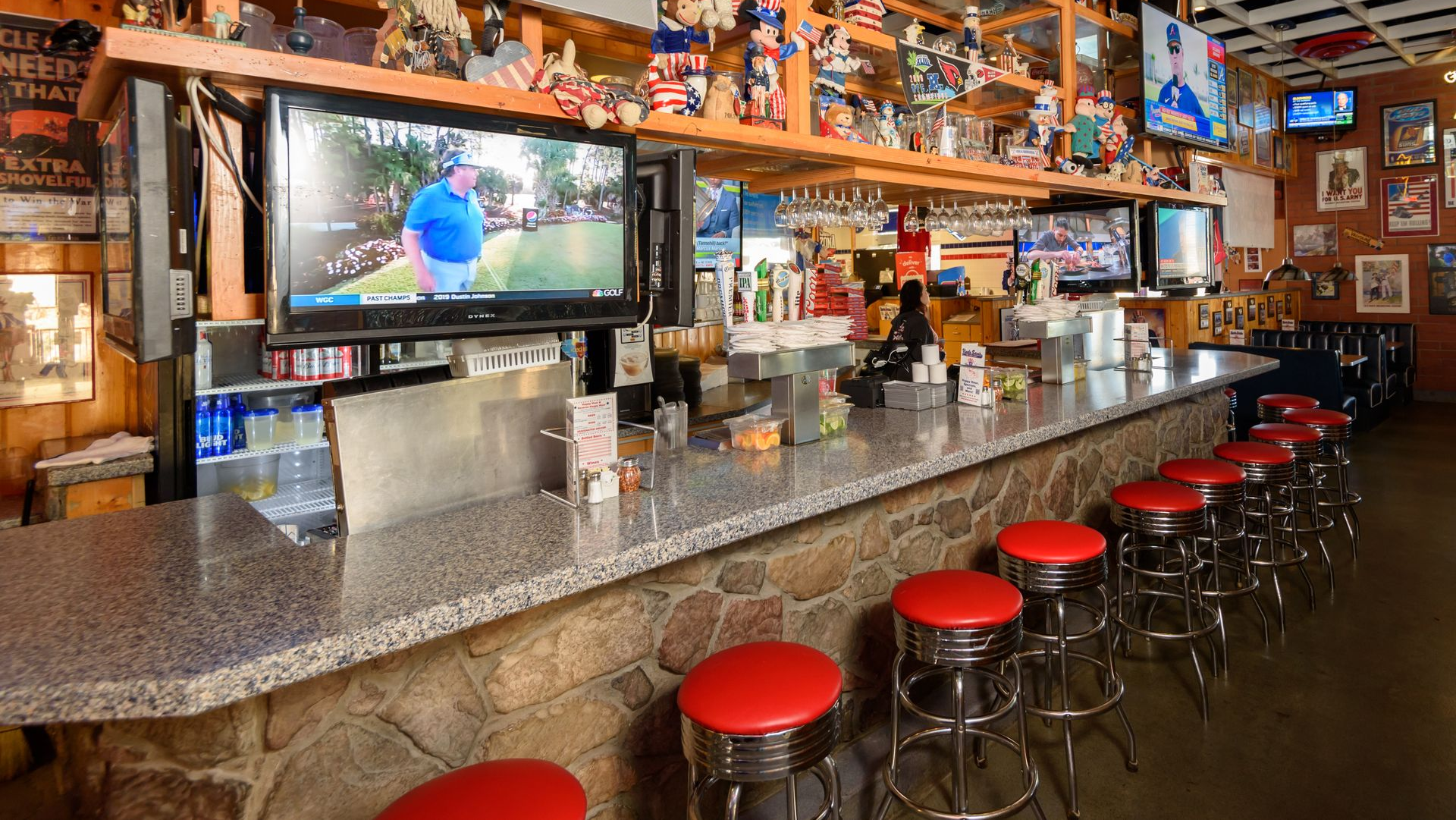 Empty sports bar with red stools, granite counter, and TVs showing a baseball game.