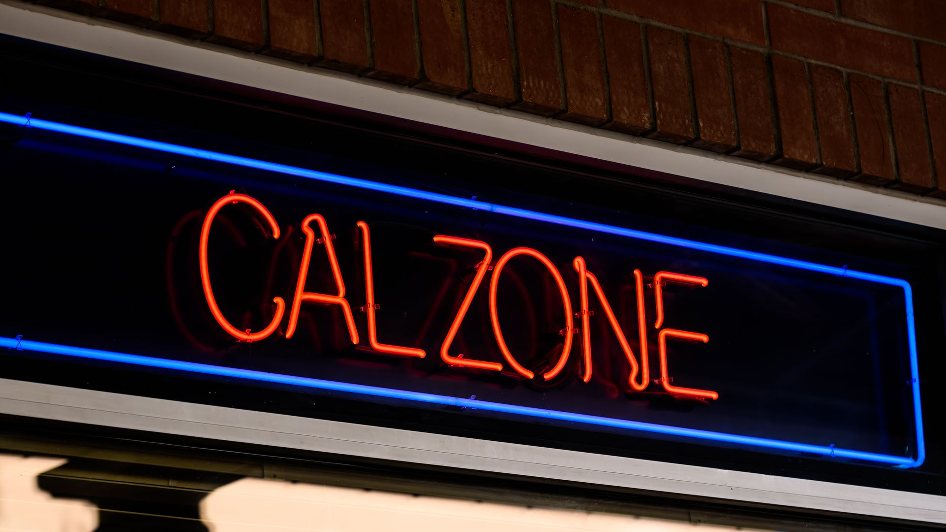 Neon red “CALZONE” sign glowing on a storefront