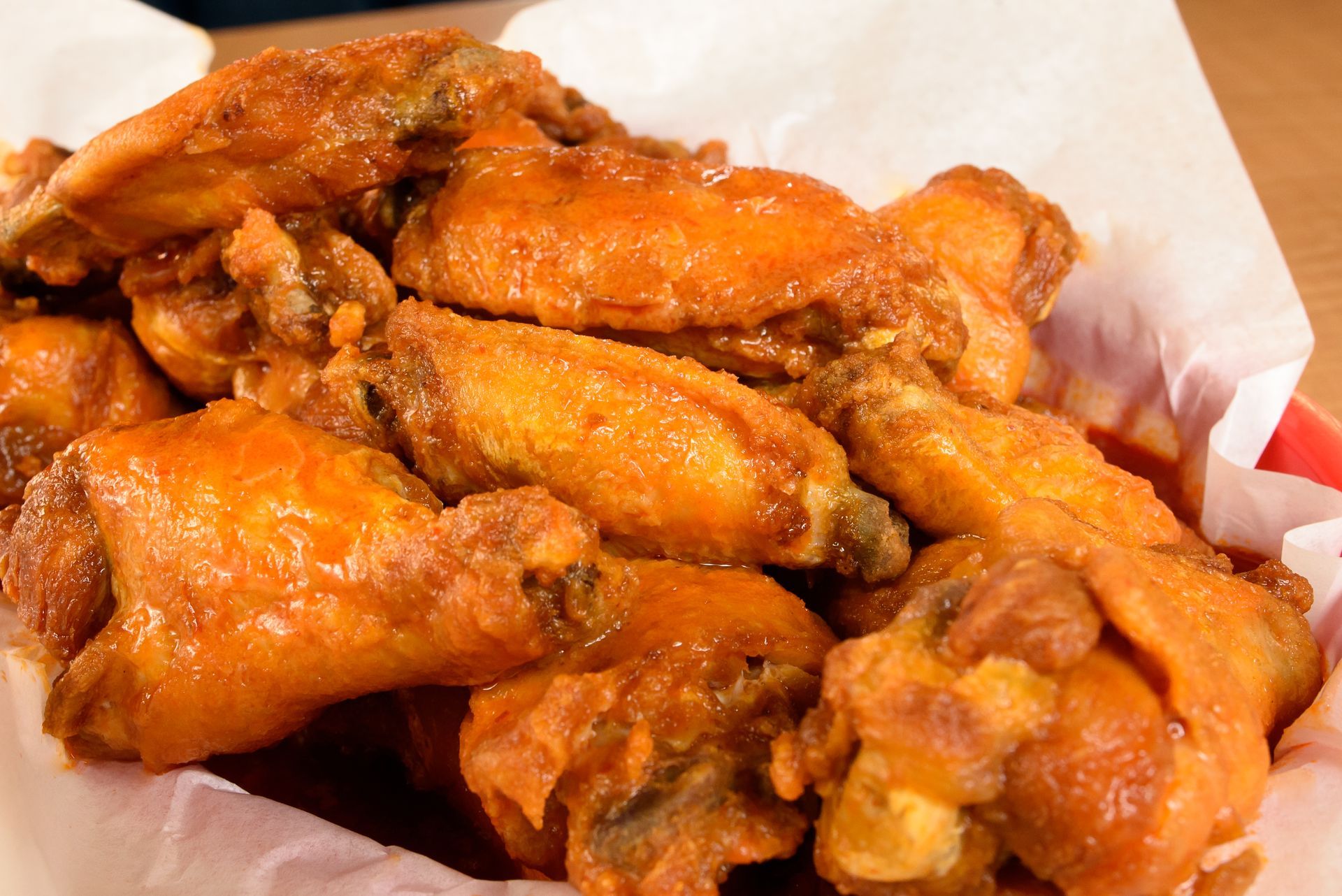 Tray of crispy fried chicken wings in orange sauce on white paper
