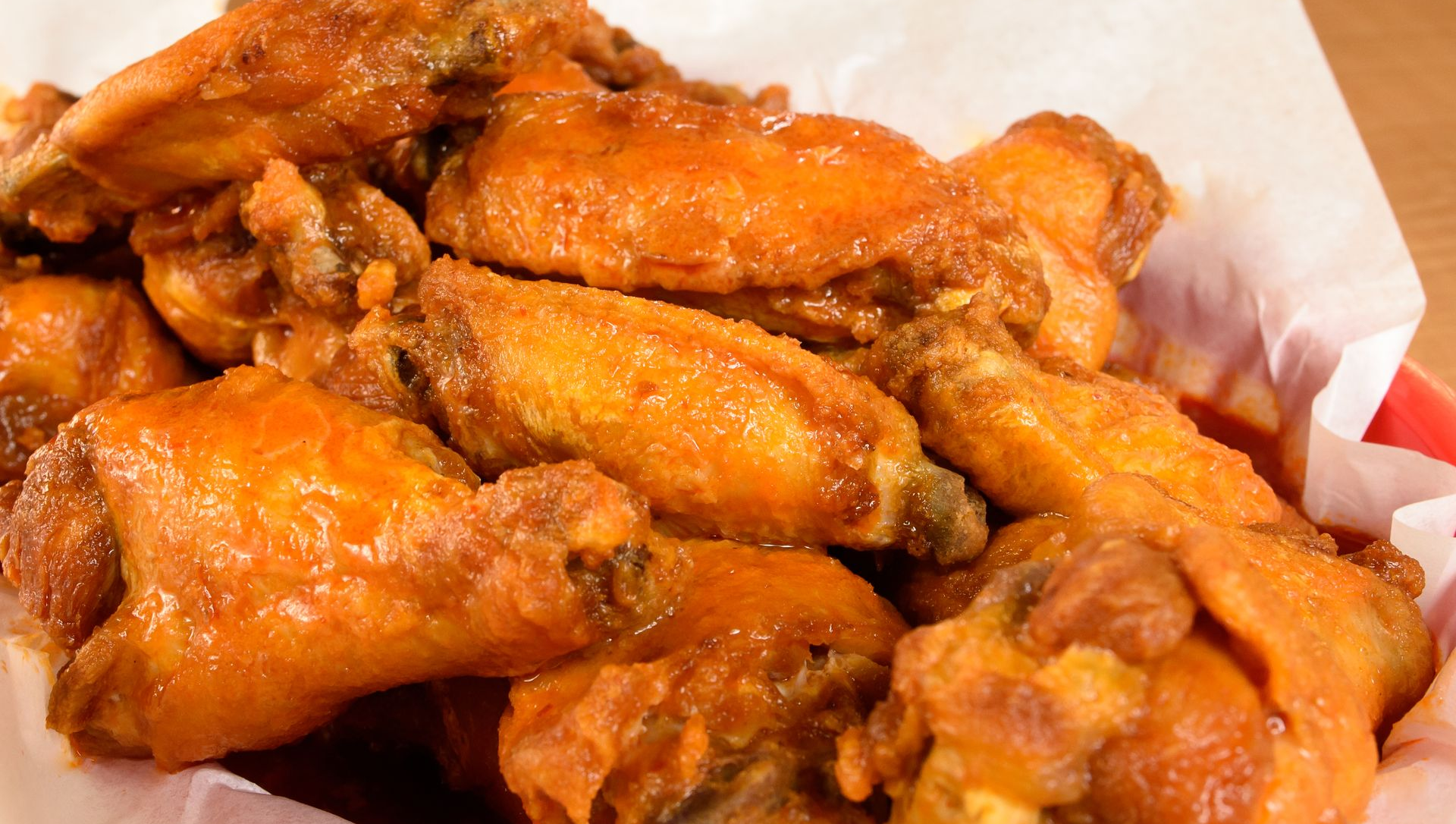 Tray of saucy orange buffalo chicken wings on white paper