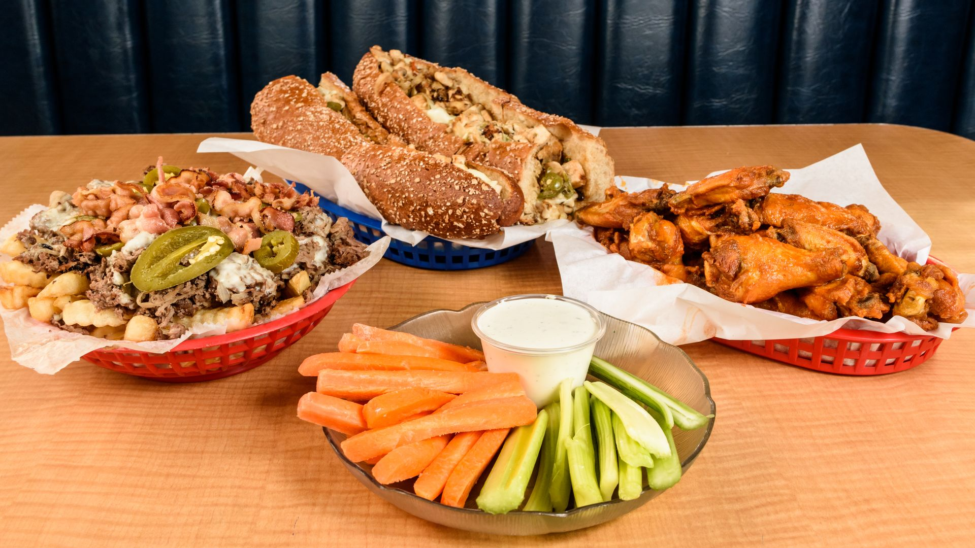 Assorted appetizers on a table: wings, sandwiches, dips, and sliced carrots and celery with ranch.