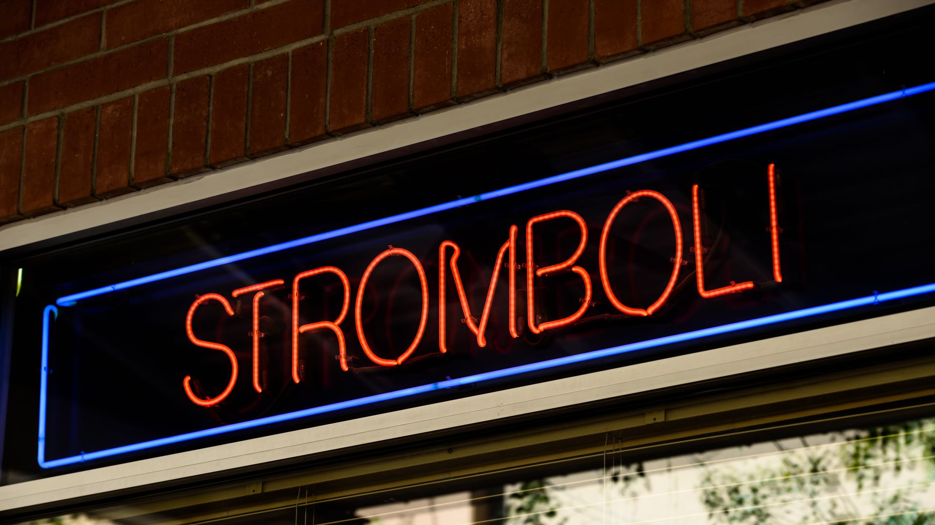 Neon “STROMBOLI” sign glowing red and blue above a storefront window