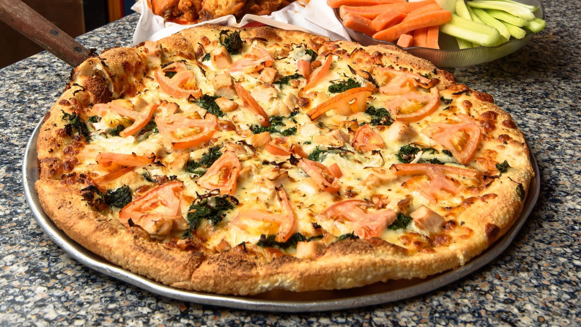 Close-up of a cheesy pizza on a granite counter with carrot and celery sticks in the background