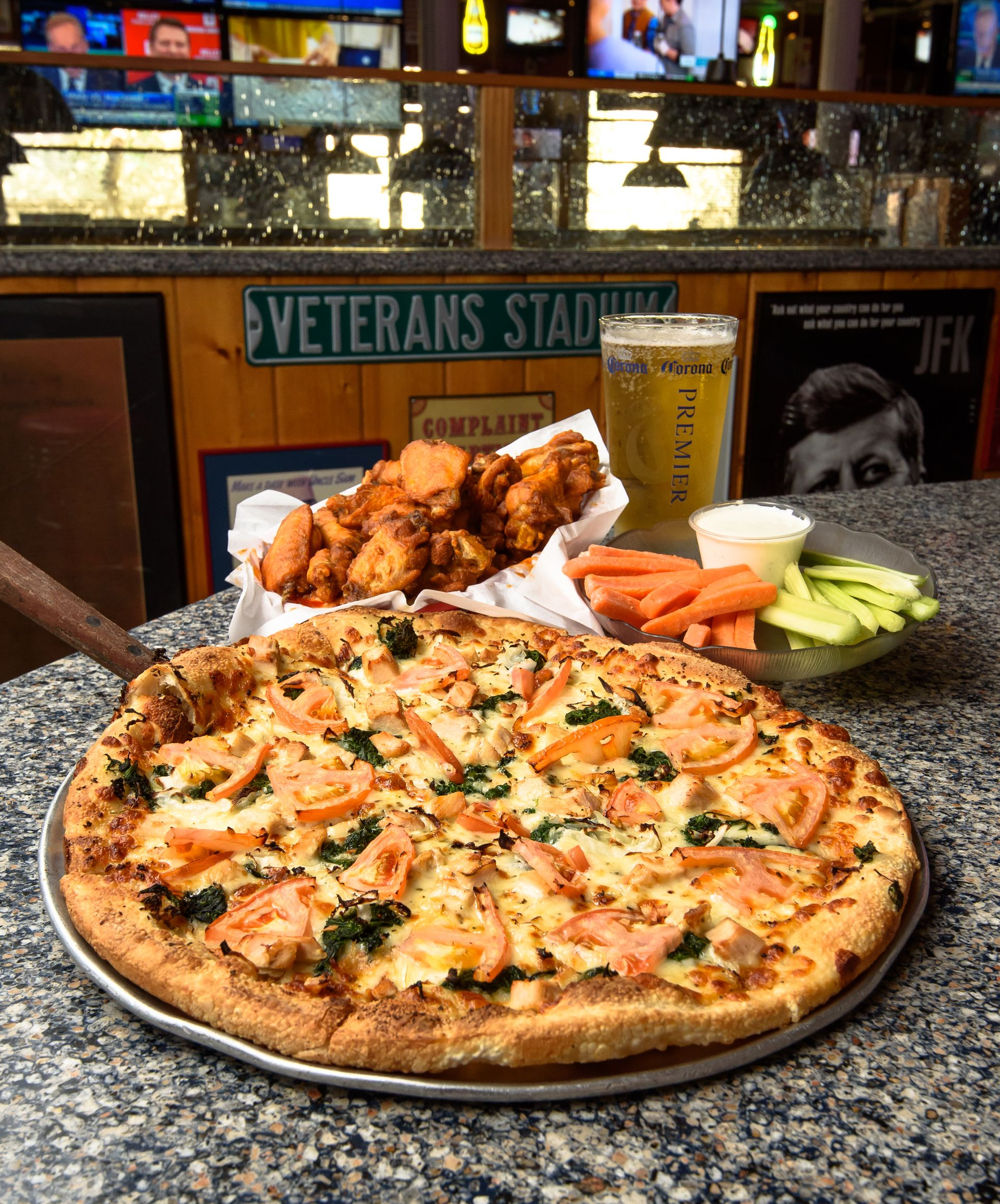 Pizza with wings, carrots, and celery on a table in a sports bar.