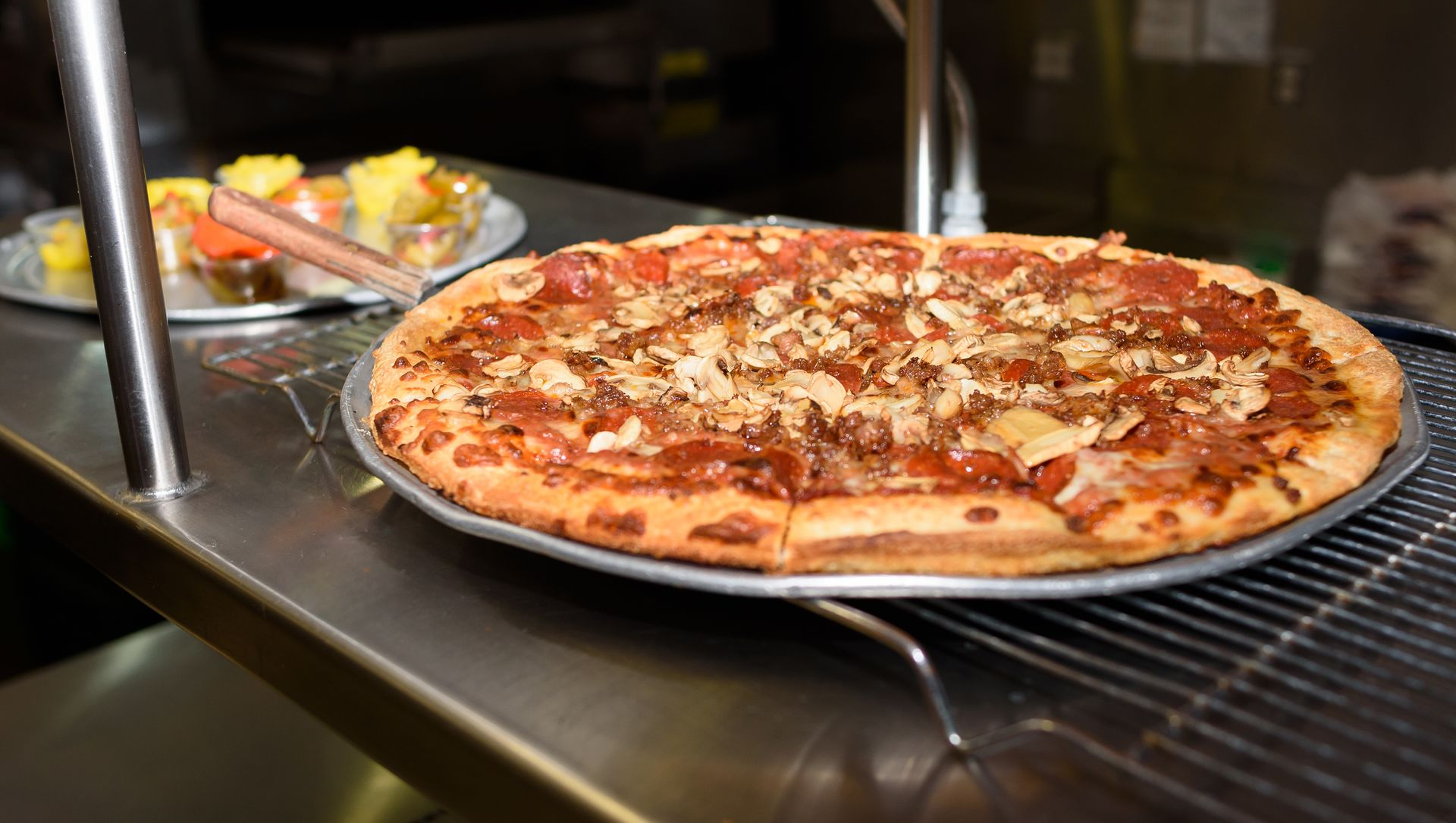 Large pepperoni pizza on a restaurant tray, with a salad blurred in the background.