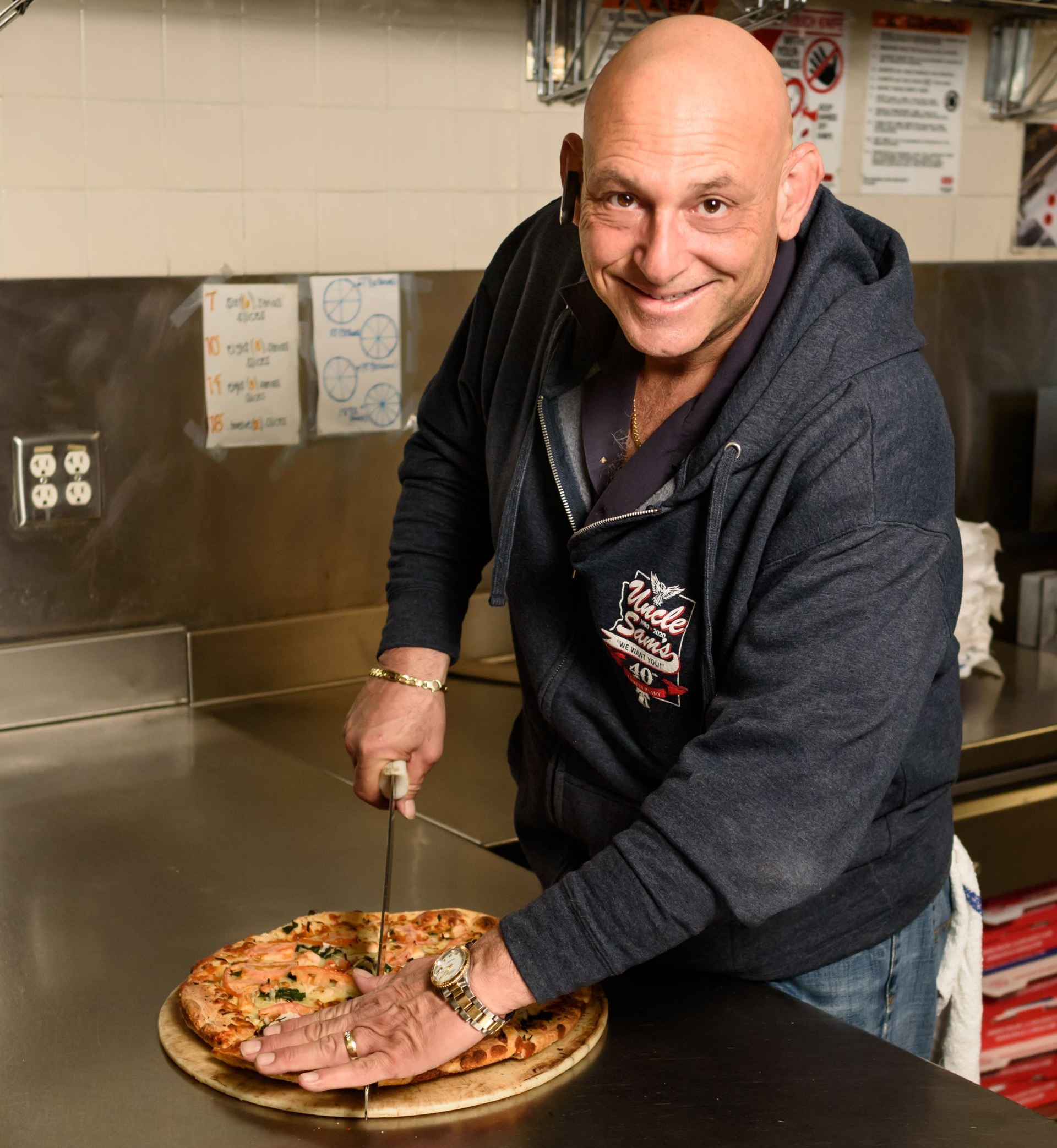 Smiling man slicing a pizza in a restaurant kitchen
