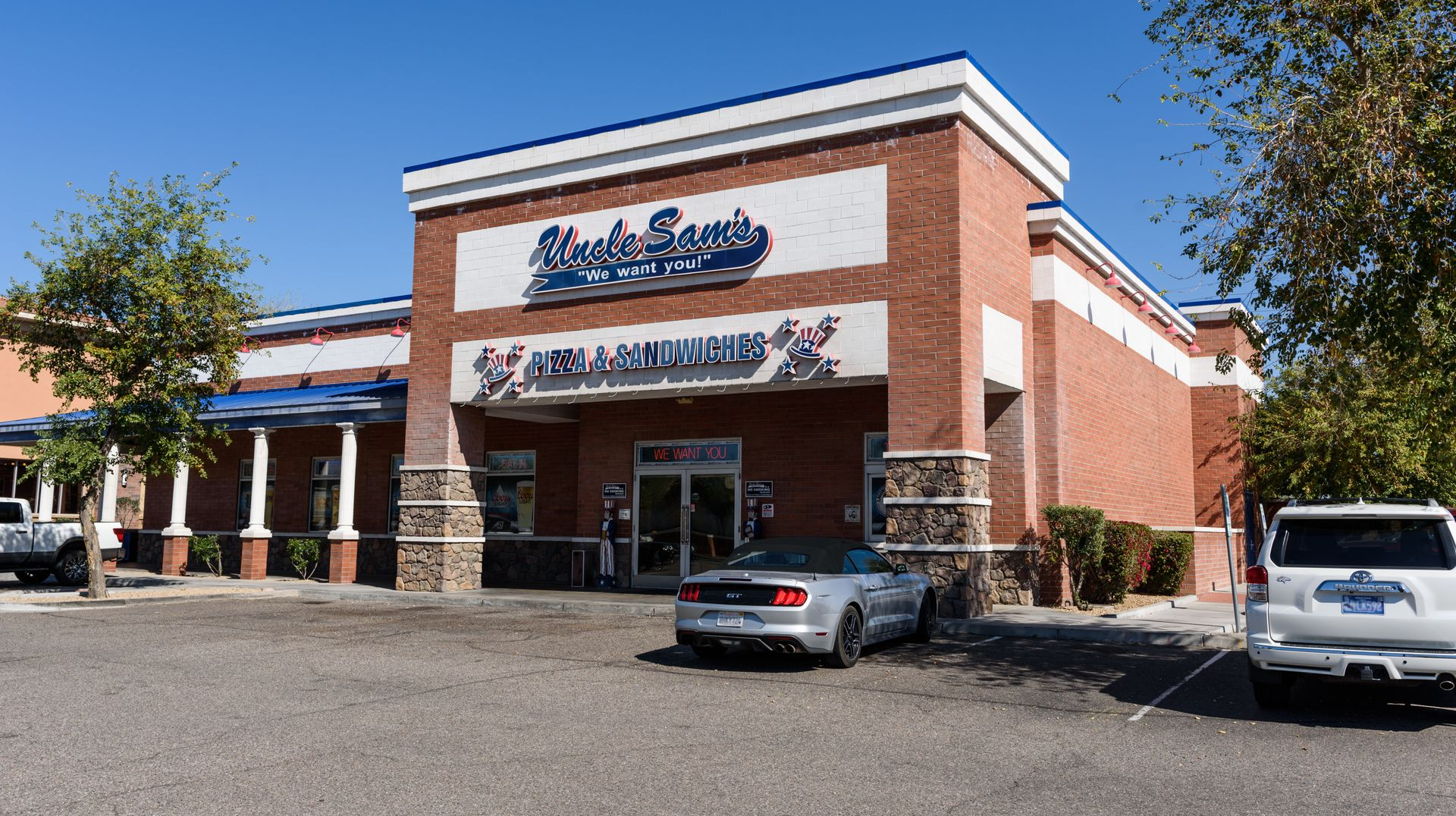 Strip mall storefront with brick facade, blue signage, and parked cars under a clear sky