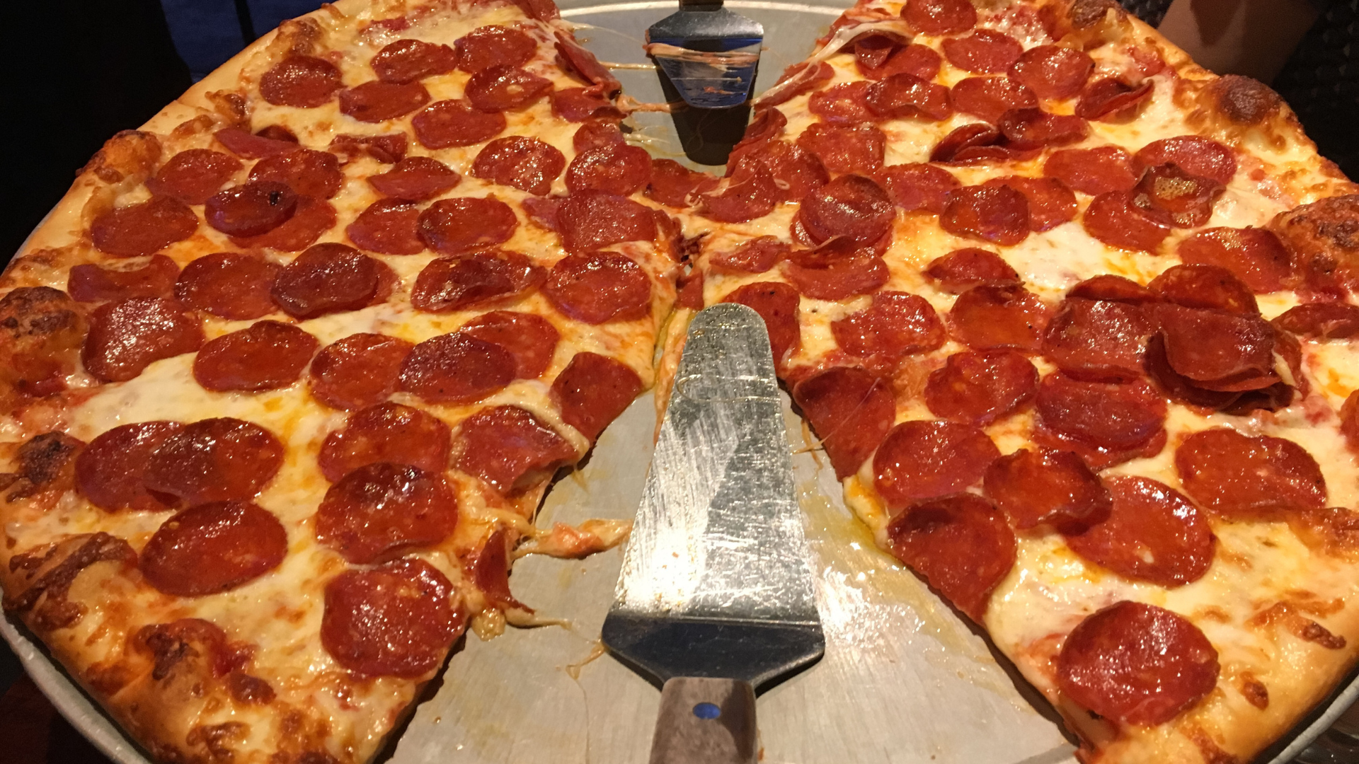 Pepperoni pizza sliced into wedges on a tray, with a spatula in the center