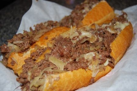 Two Philadelphia cheesesteaks topped with melted cheese and sautéed onions served on a hoagie roll on parchment paper.