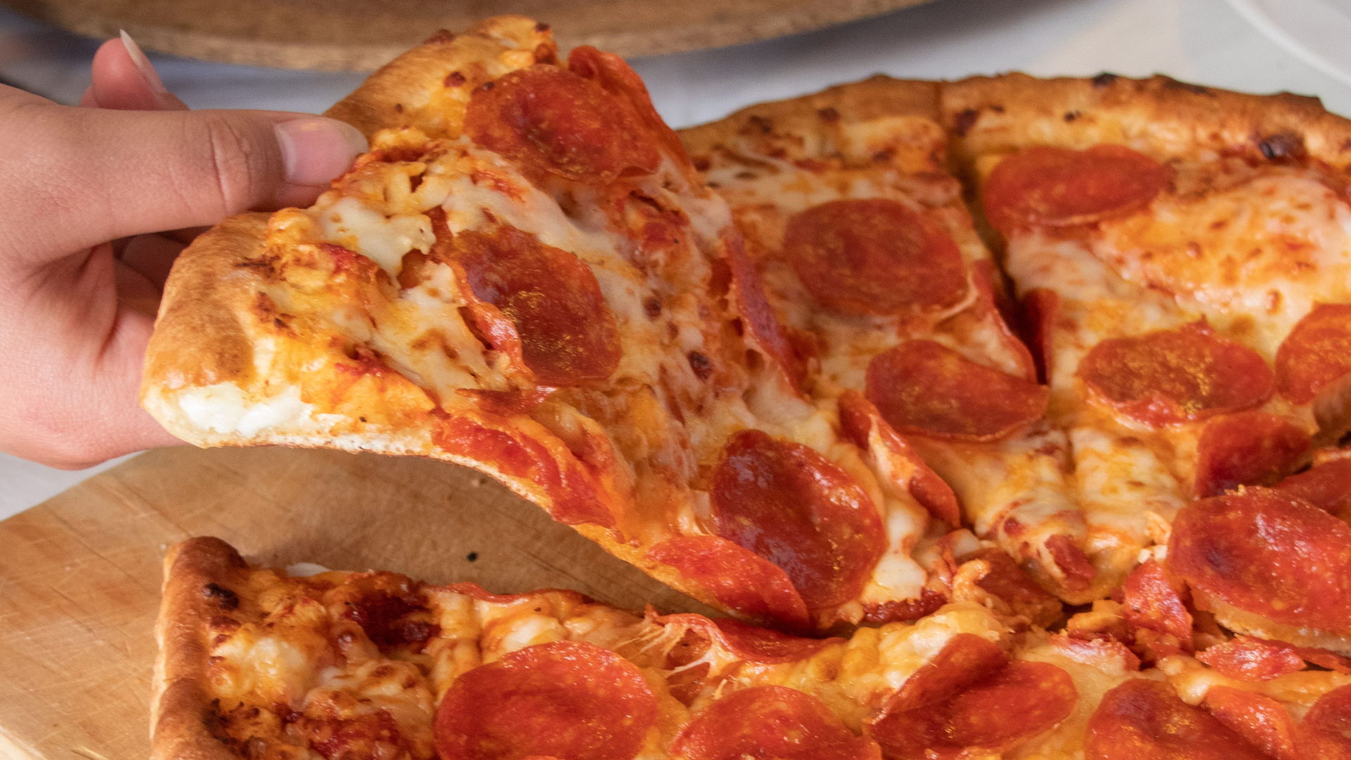 Hand lifting a pepperoni pizza slice from a cheese and pepperoni pizza on a wooden tray