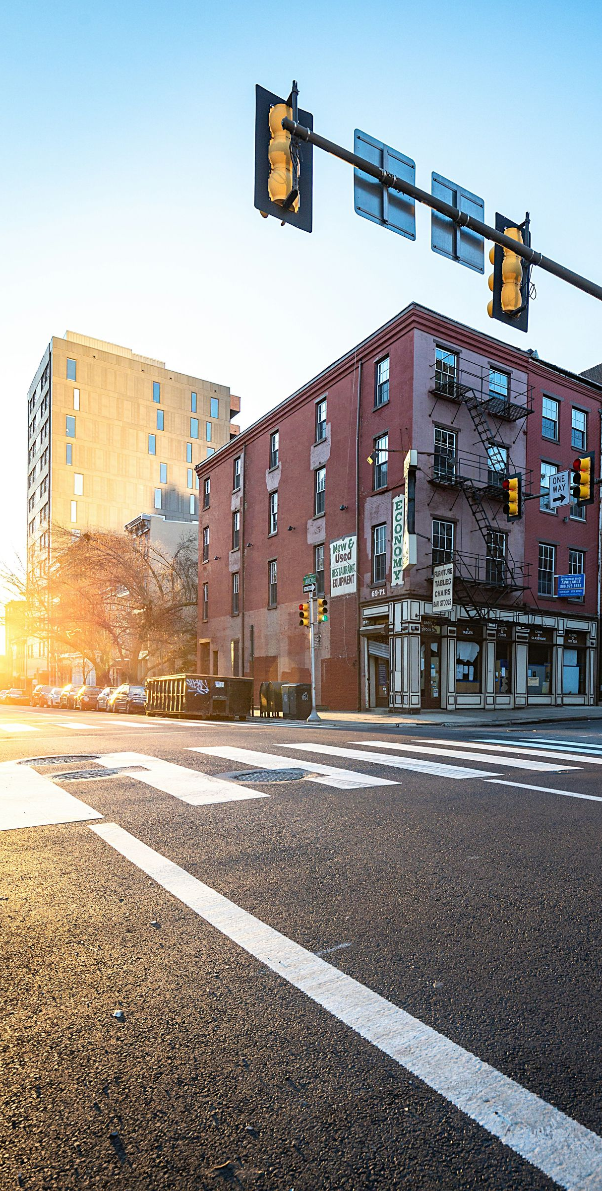 Sunlit city street intersection with brick buildings, traffic lights, and crosswalks at dusk