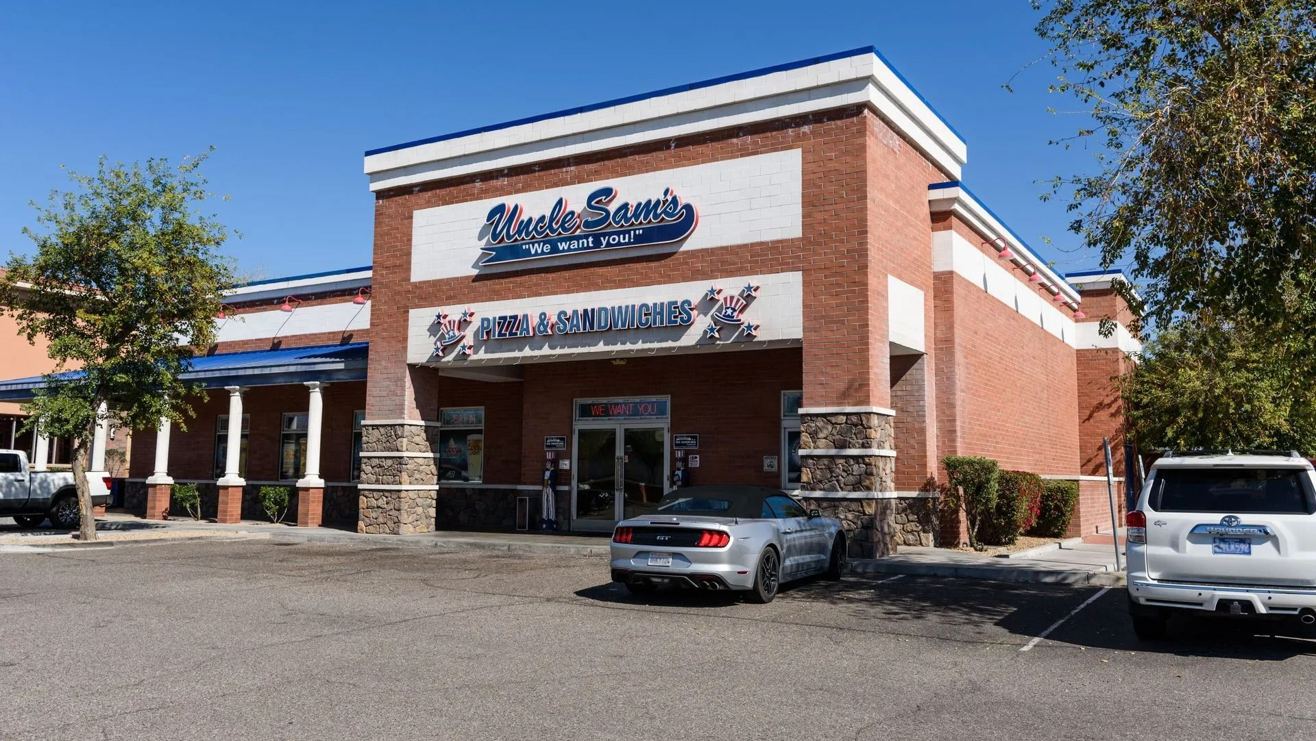 Strip mall storefront with brick facade, blue signage, and parked cars on a sunny day