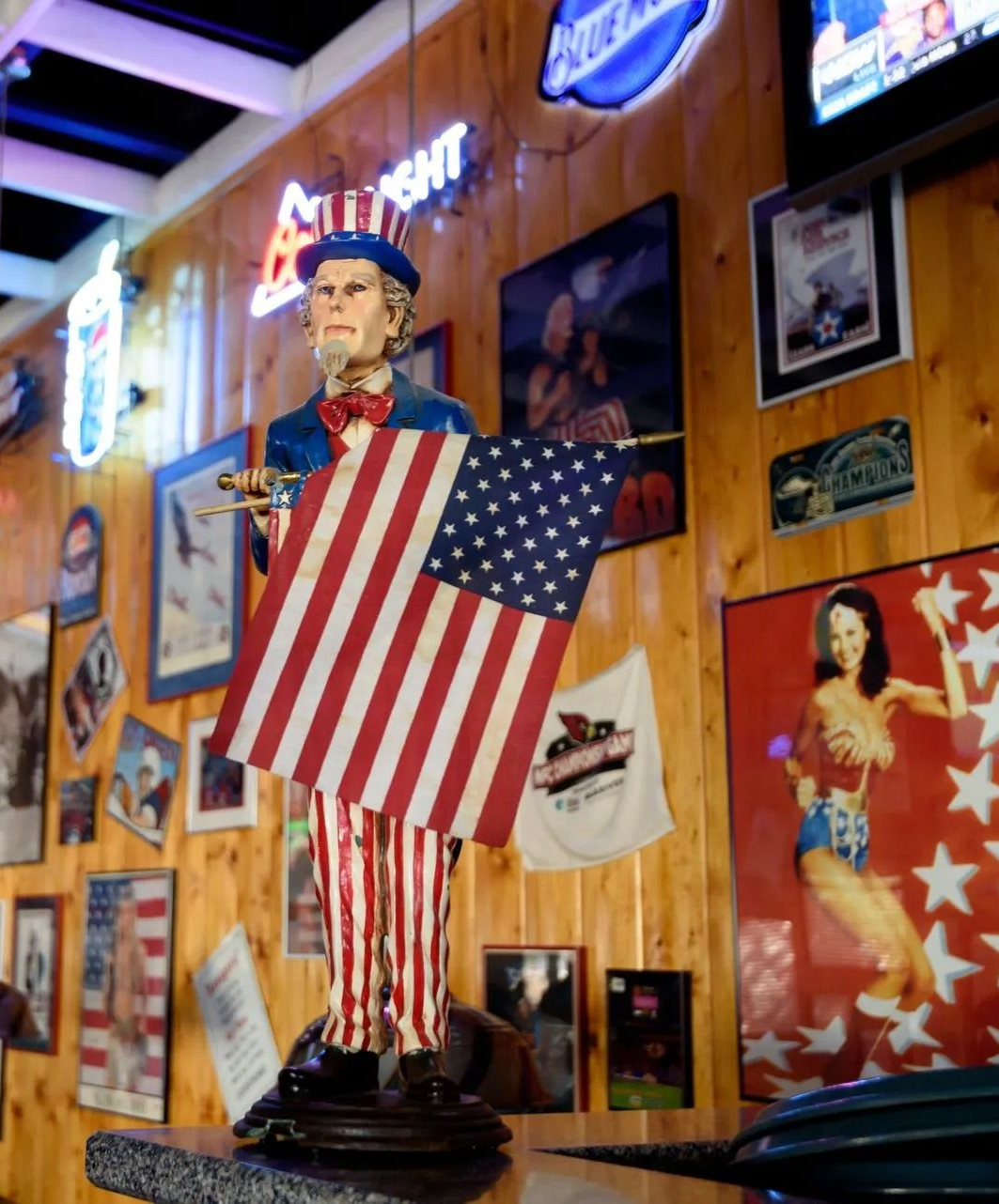 Statue holding a large American flag in a colorful, poster-covered bar interior