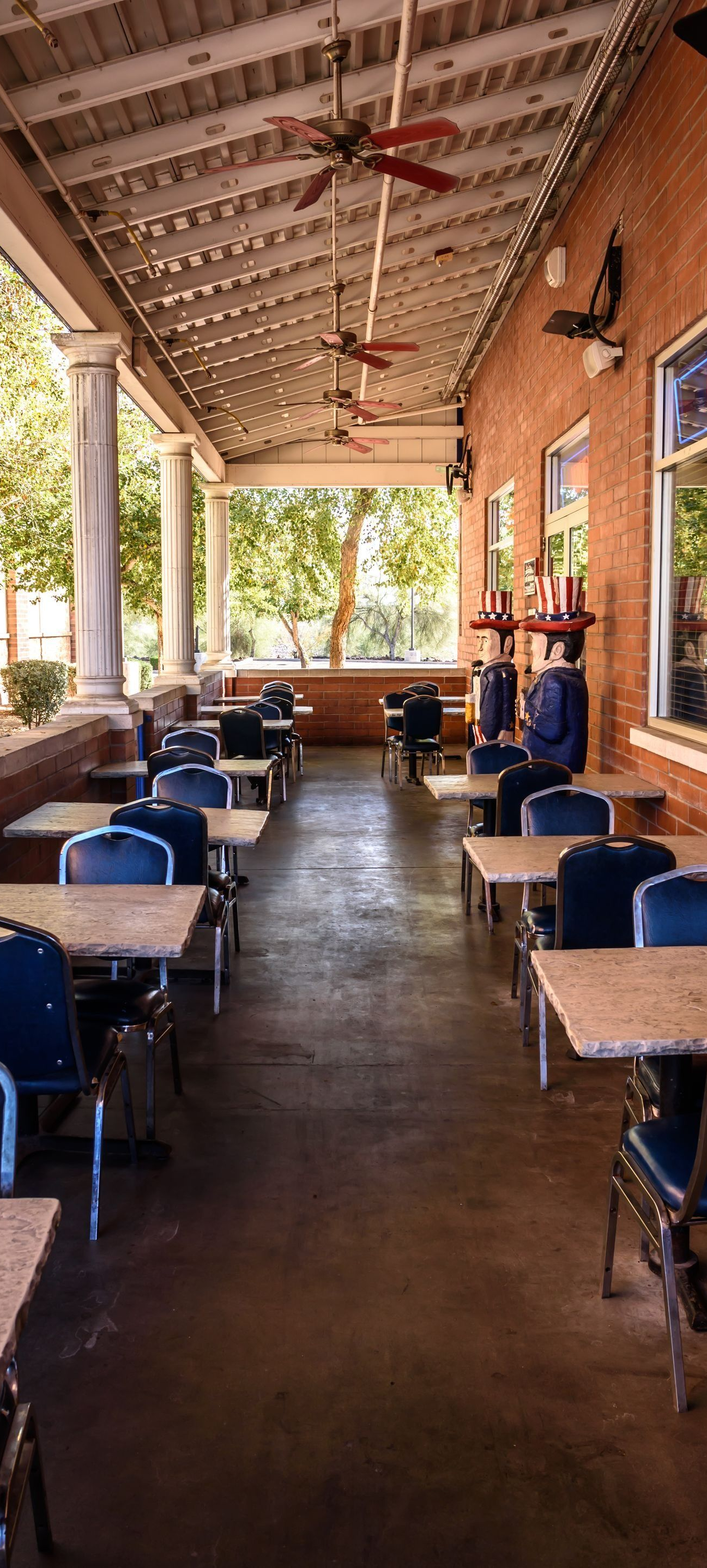 A covered patio with dining tables and blue chairs stretching alongside a brick building.