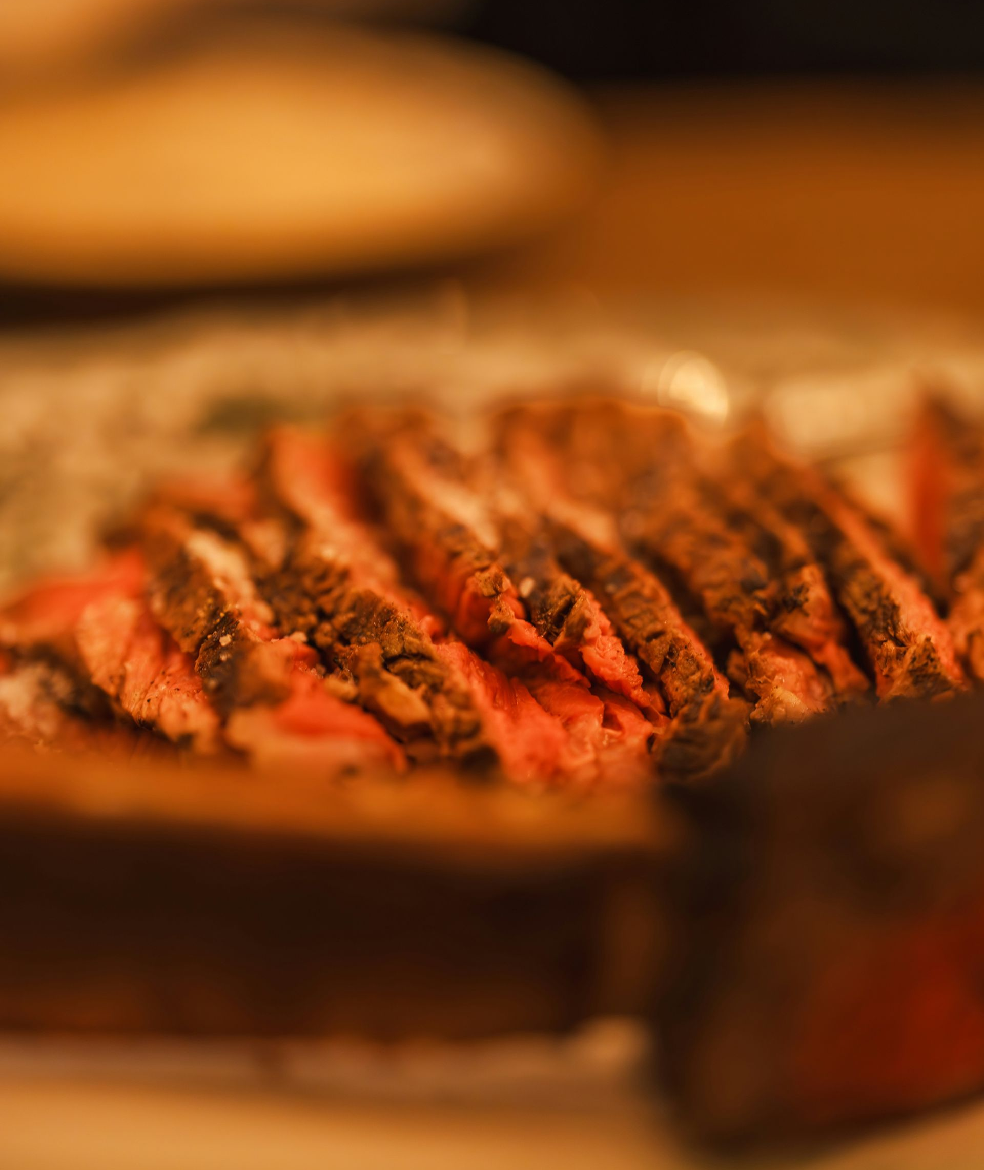 A platter of sliced, medium-rare steak served on a dark, rustic wooden surface in dim lighting.