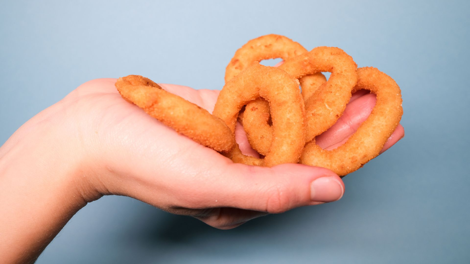 Hand holding several onion rings against a light blue background