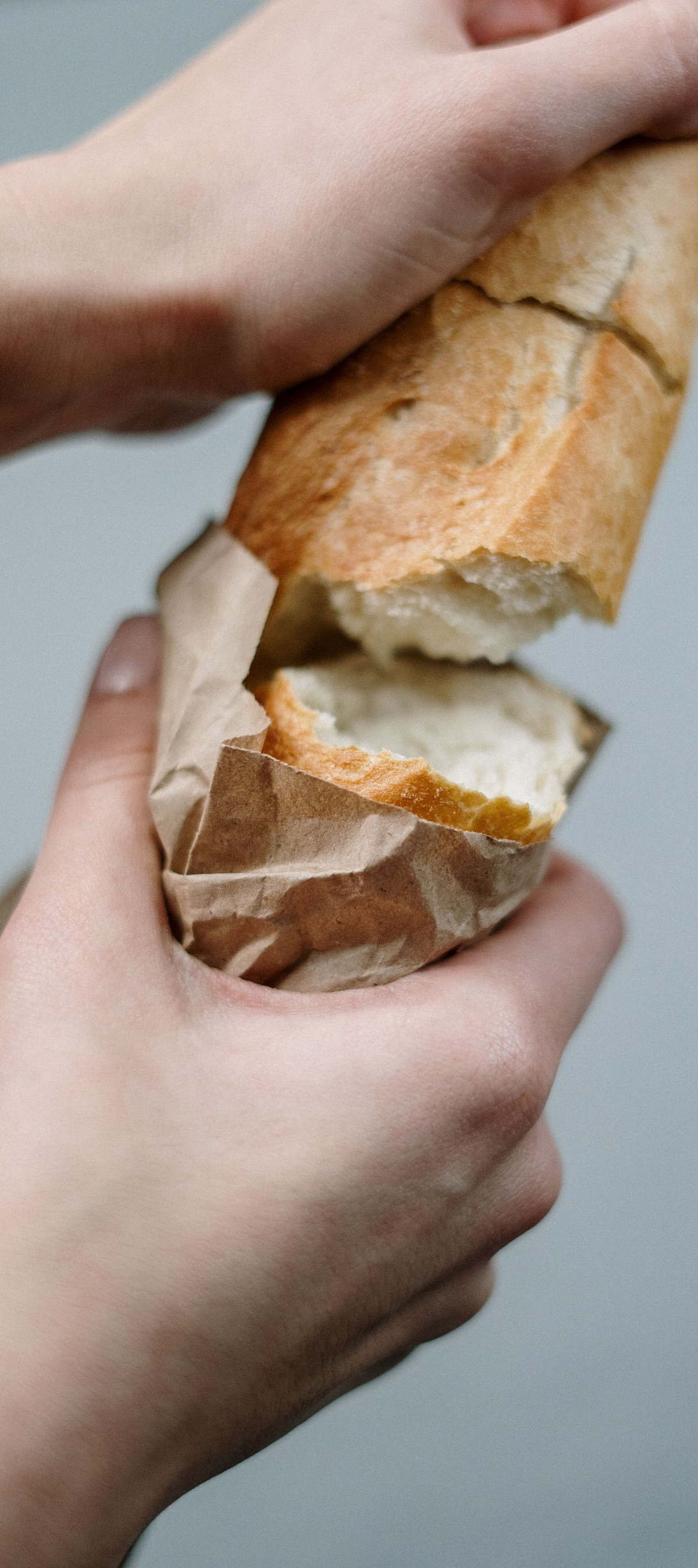 Hands breaking a crusty baguette over a gray background