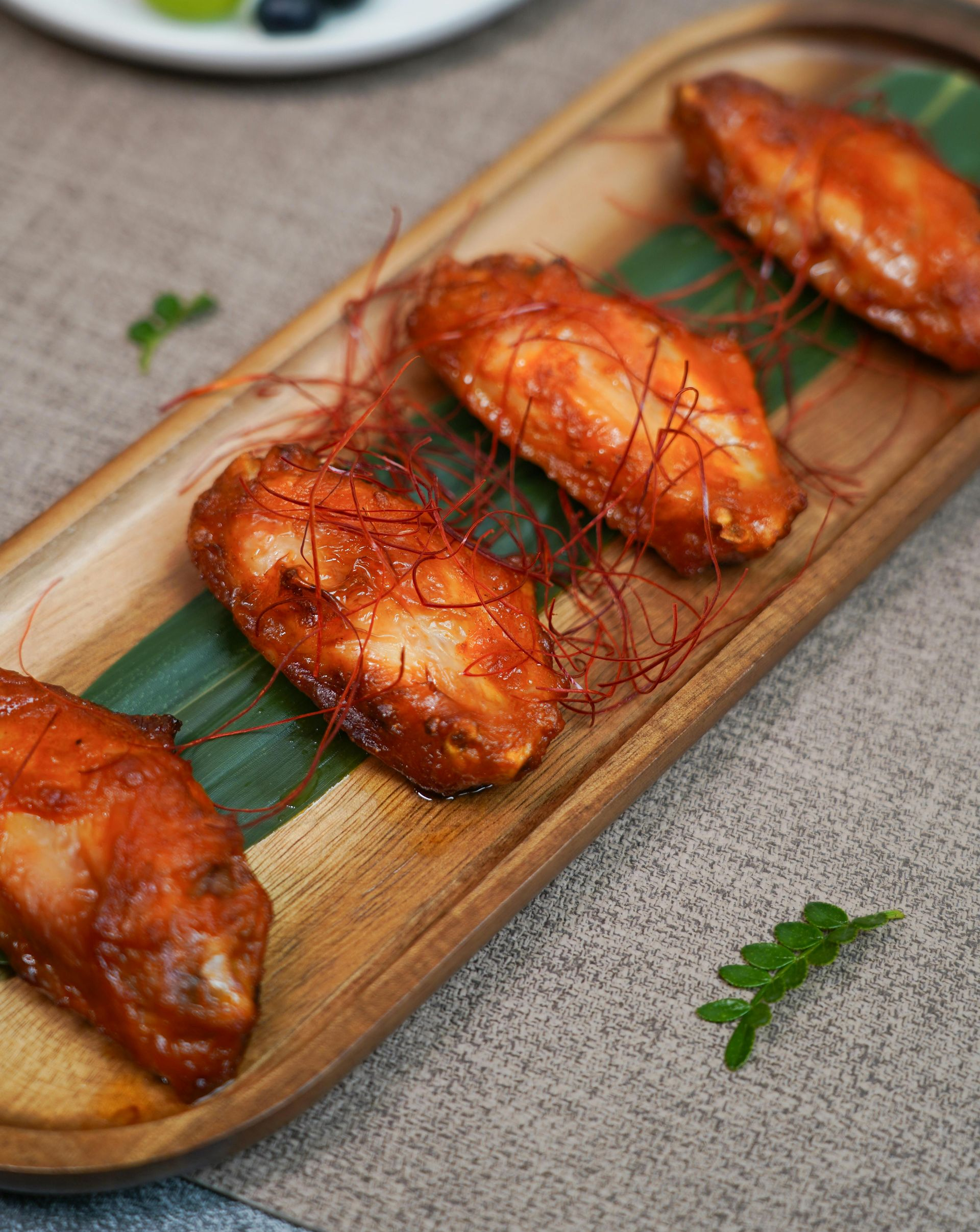 Glazed roasted chicken drumsticks on a wooden serving tray with green leaves and side garnish