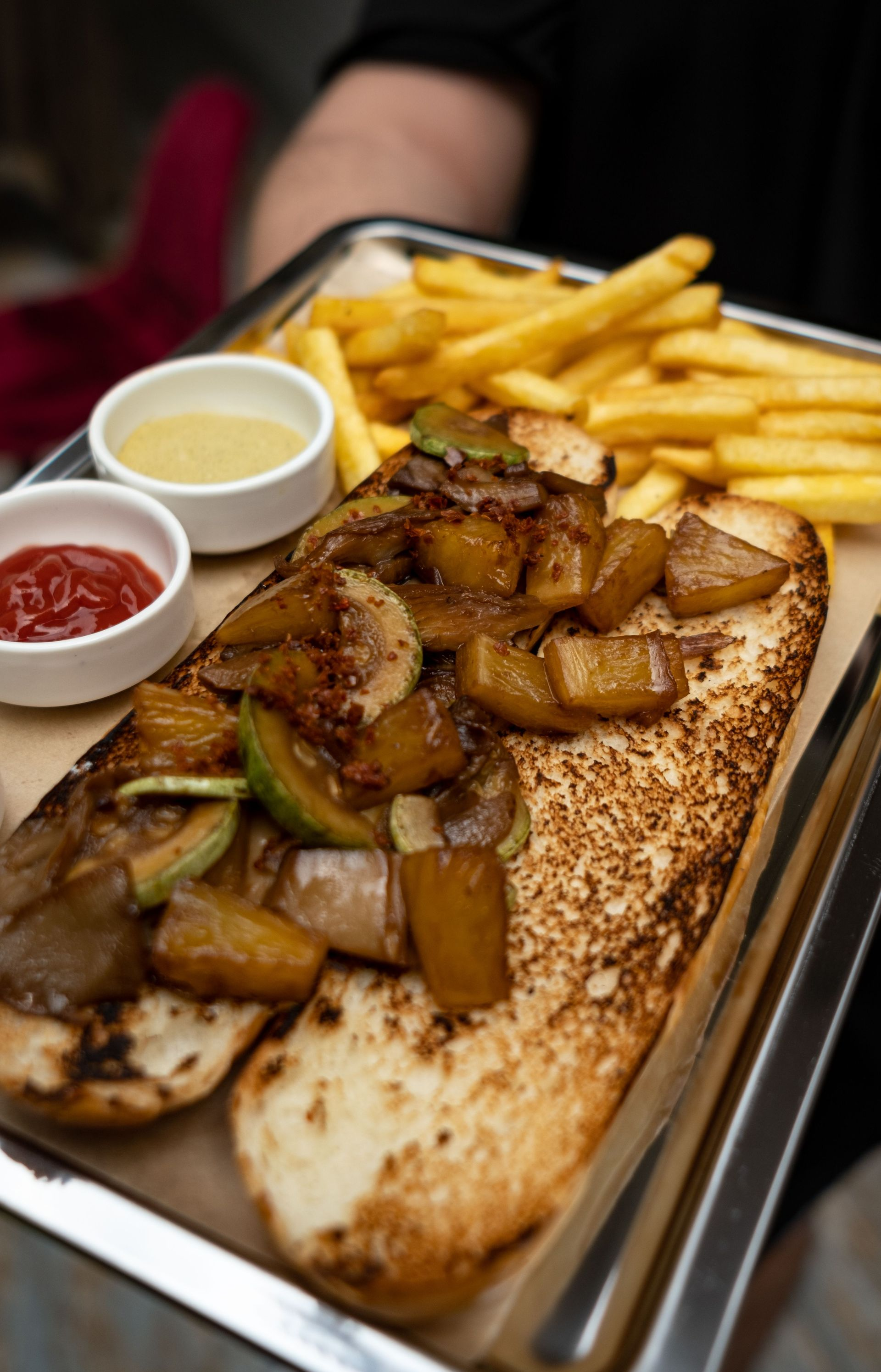 Grilled meat and potatoes on flatbread with fries and dipping sauces on a metal tray