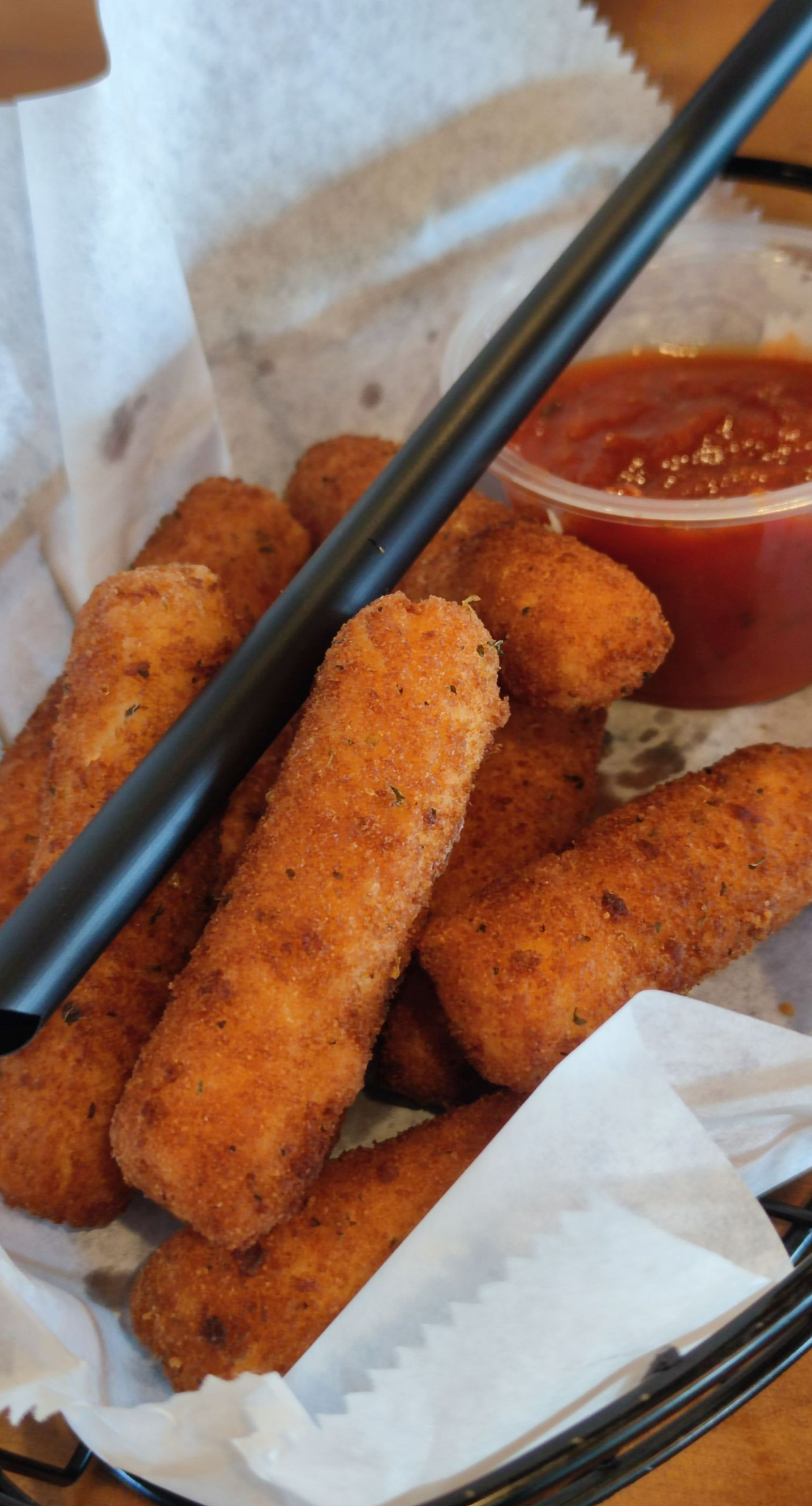 Basket of breaded mozzarella sticks with marinara sauce and chopsticks.