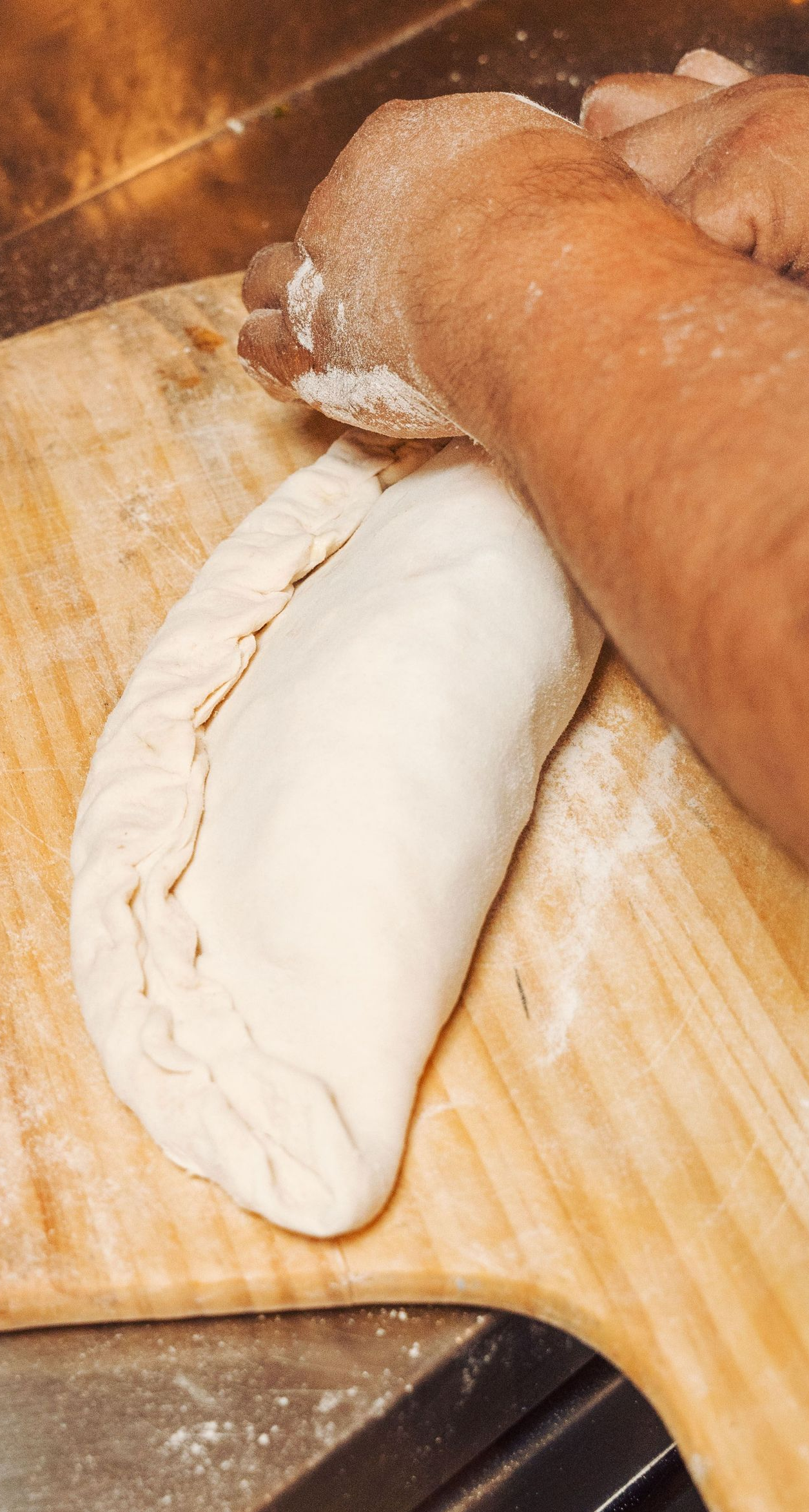 Hands shaping dough on a floured wooden board with a rolling pin nearby