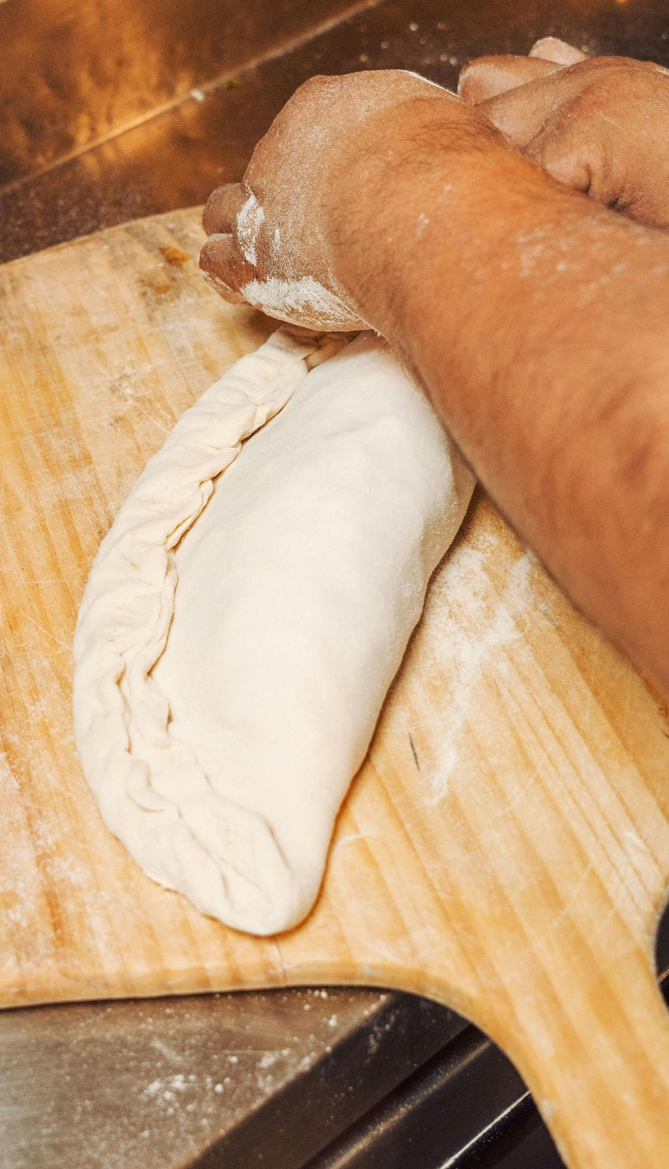 Hands kneading white dough on a wooden cutting board in a kitchen sink area