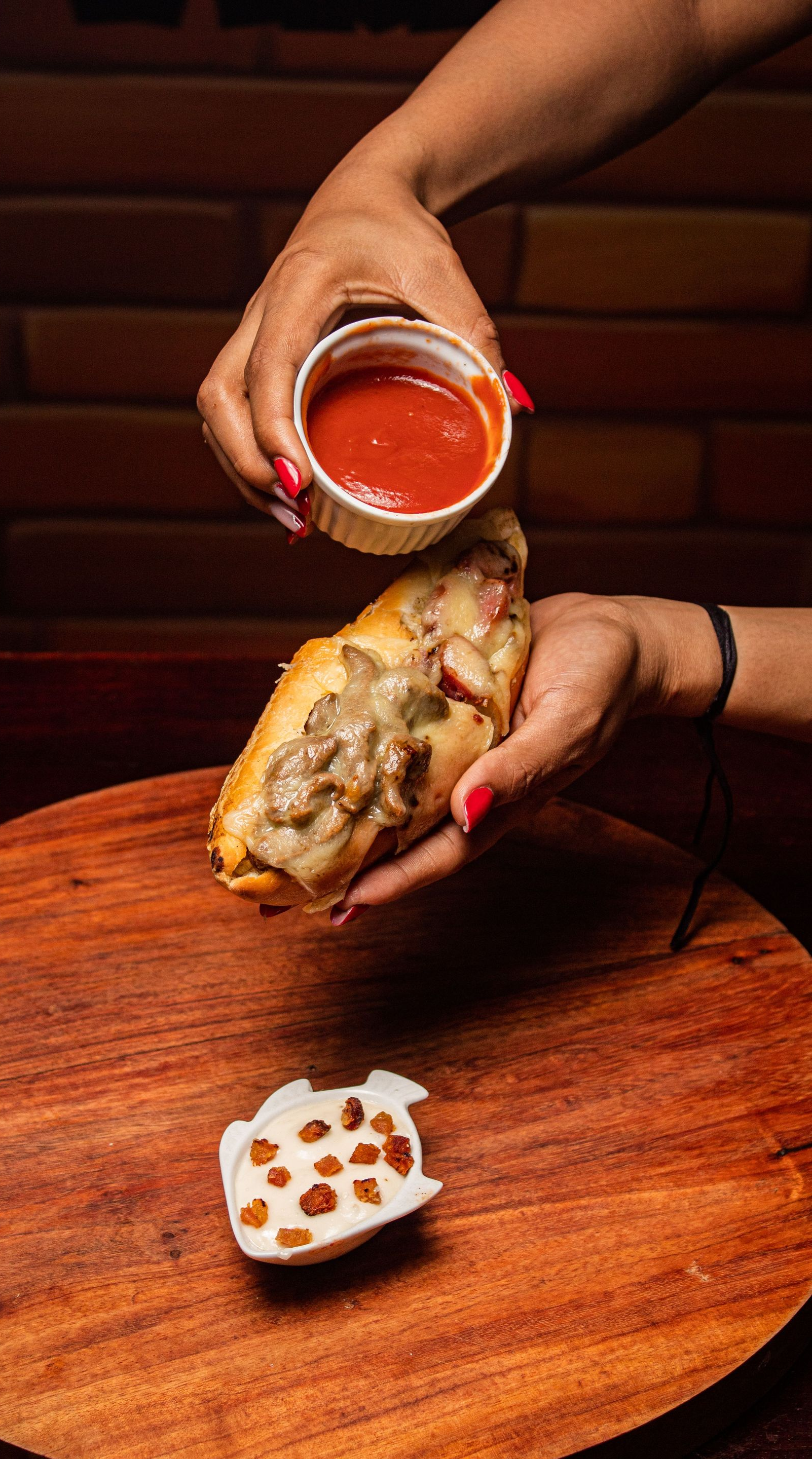 Hands pouring red sauce over a fried stuffed pastry on a wooden table