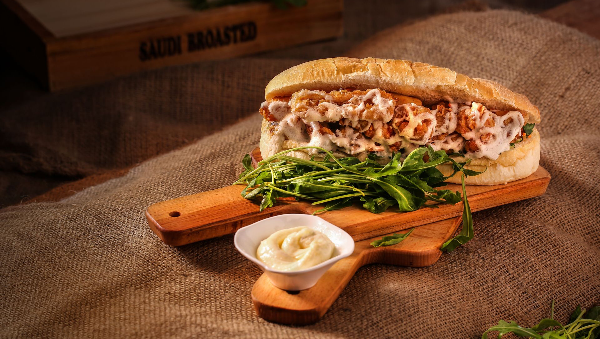 Sandwich with greens and creamy sauce on a wooden board, set on burlap in warm rustic lighting