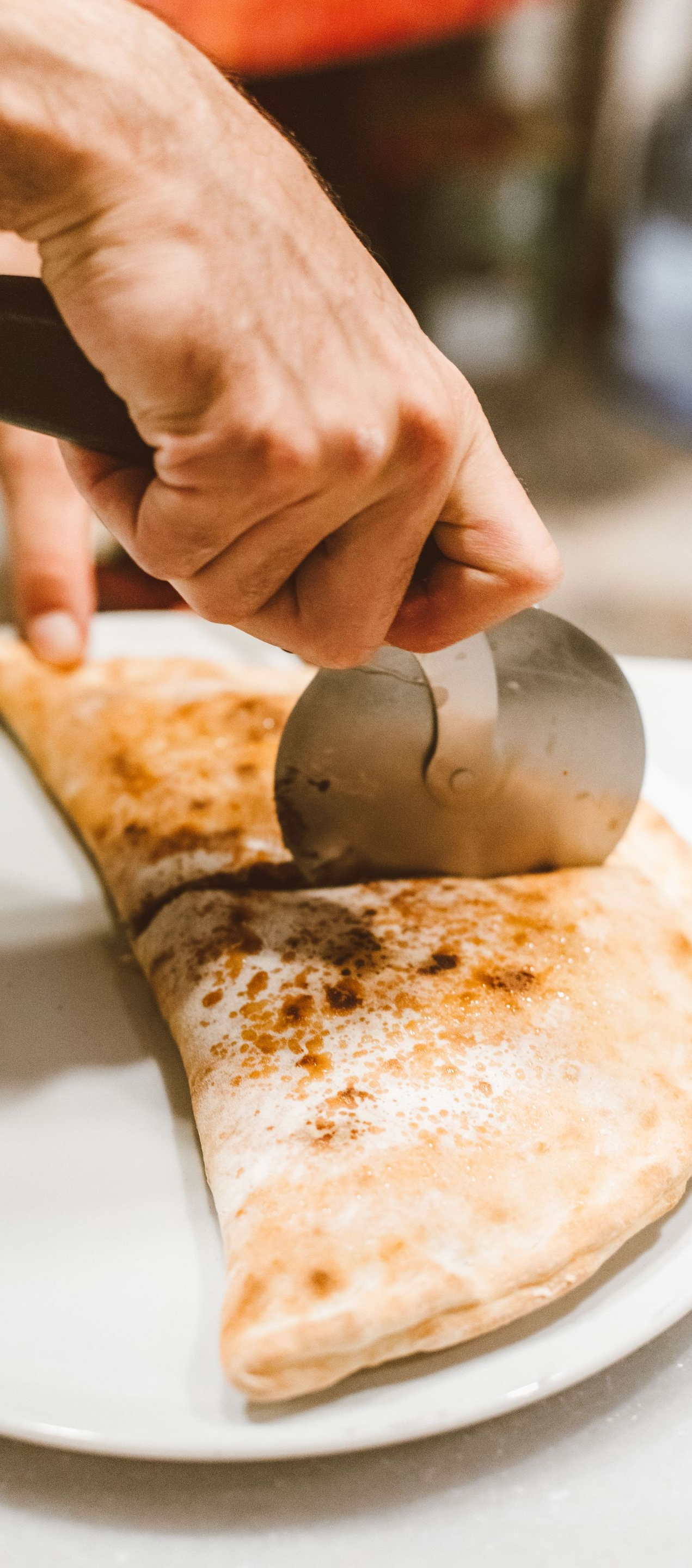Hand using a pizza cutter to slice a folded pizza on a white plate