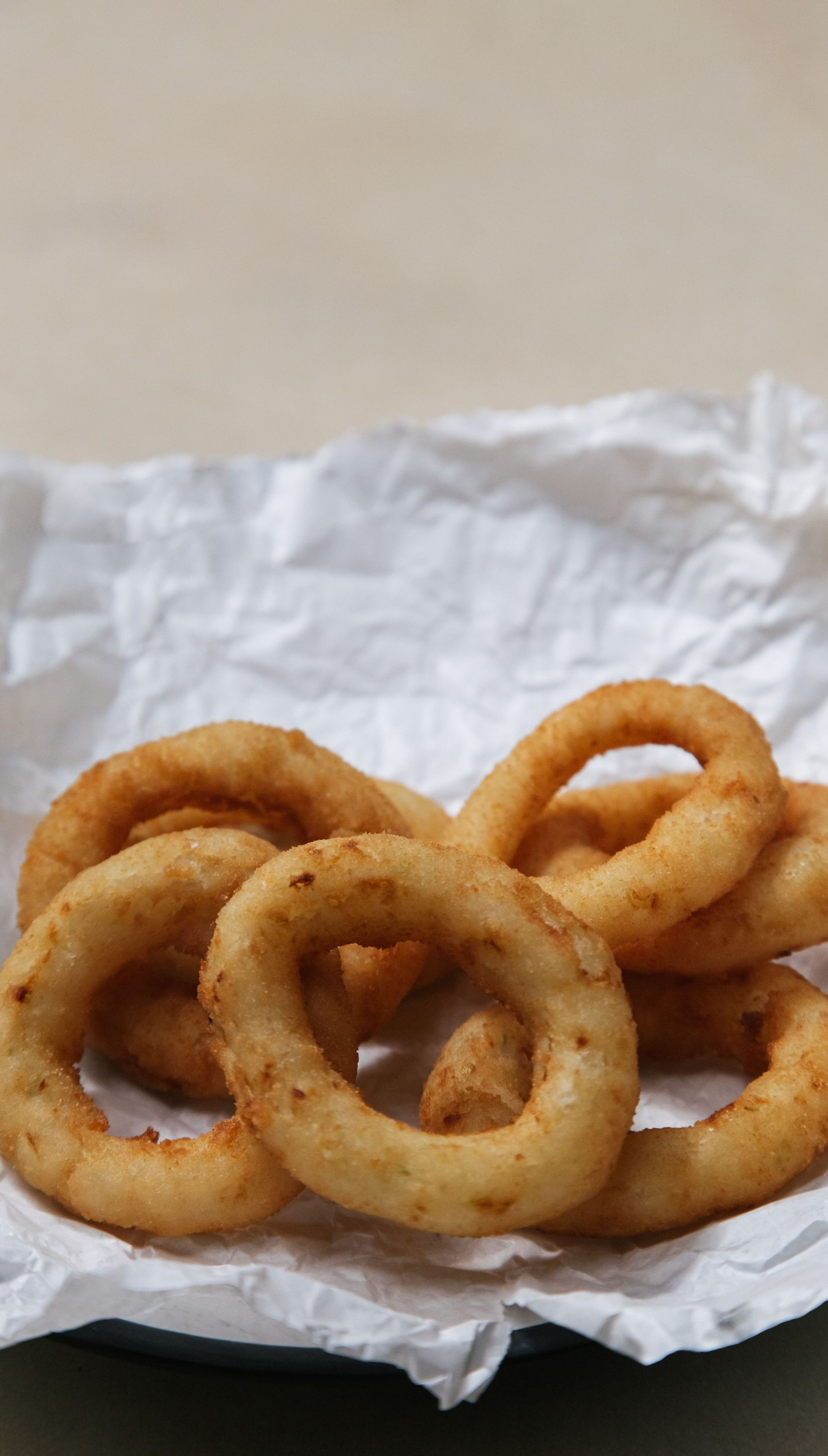 On crumpled white paper, several golden-brown onion rings are stacked together.