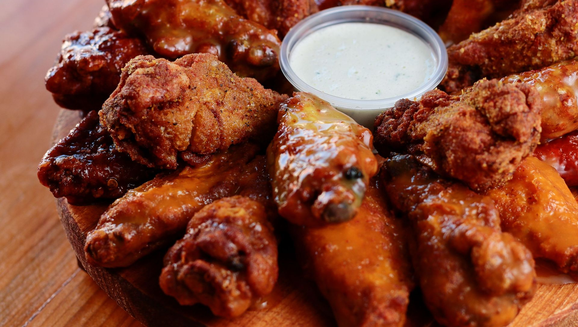 Plate of saucy chicken wings with a cup of ranch dip on a wooden tray