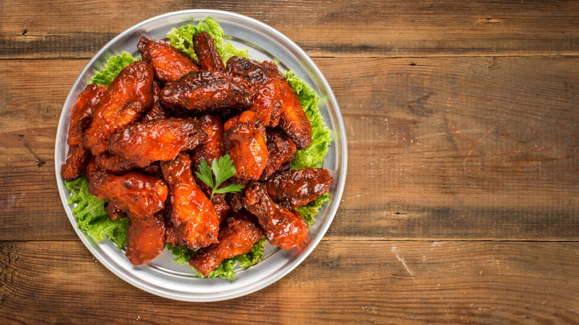 A bowl of glazed chicken wings on lettuce, served on a wooden table.
