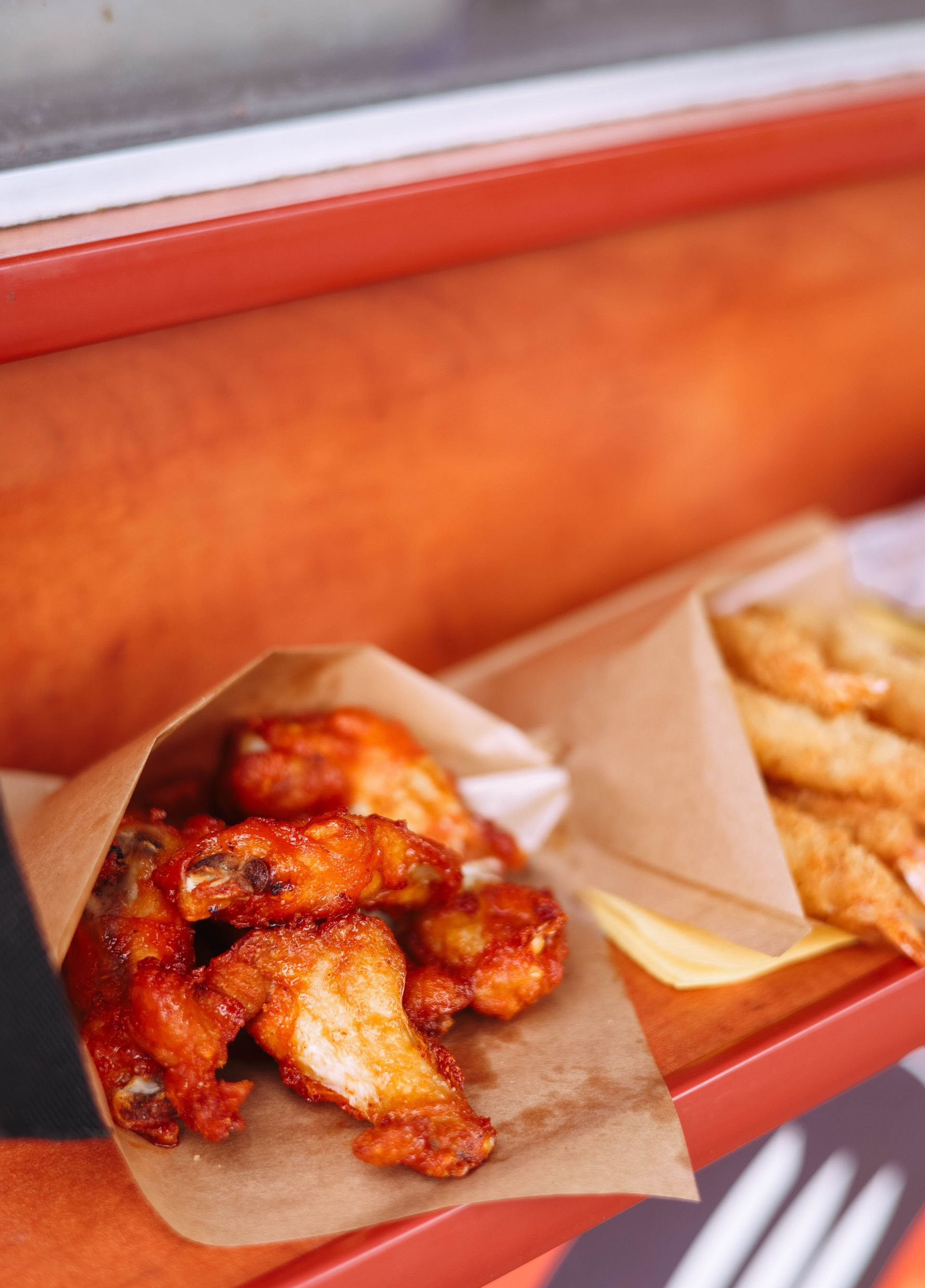 Assorted glazed fried chicken pieces in paper trays on a counter, with a red backdrop