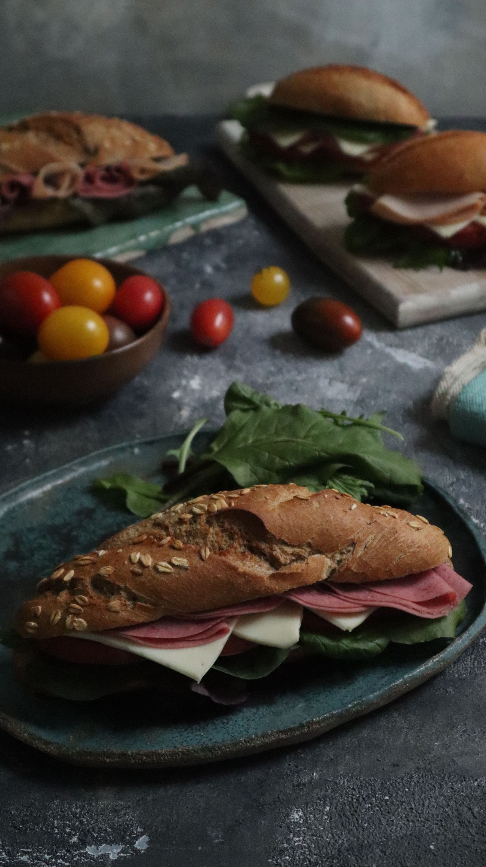 Assorted sandwiches and cherry tomatoes on dark plates, styled on a rustic table