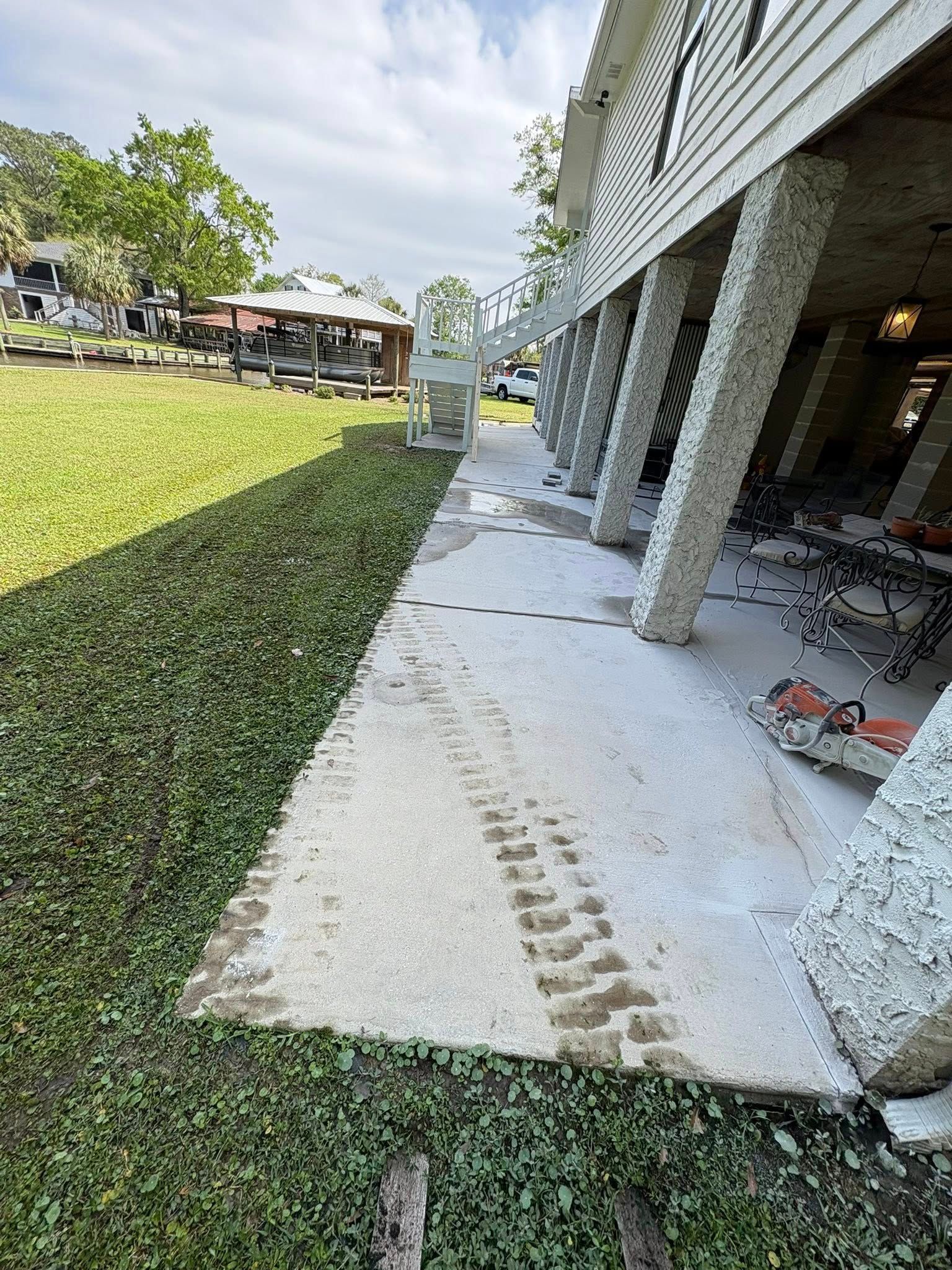 A concrete patio with heavy tire tracks underneath an elevated building beside a green lawn.