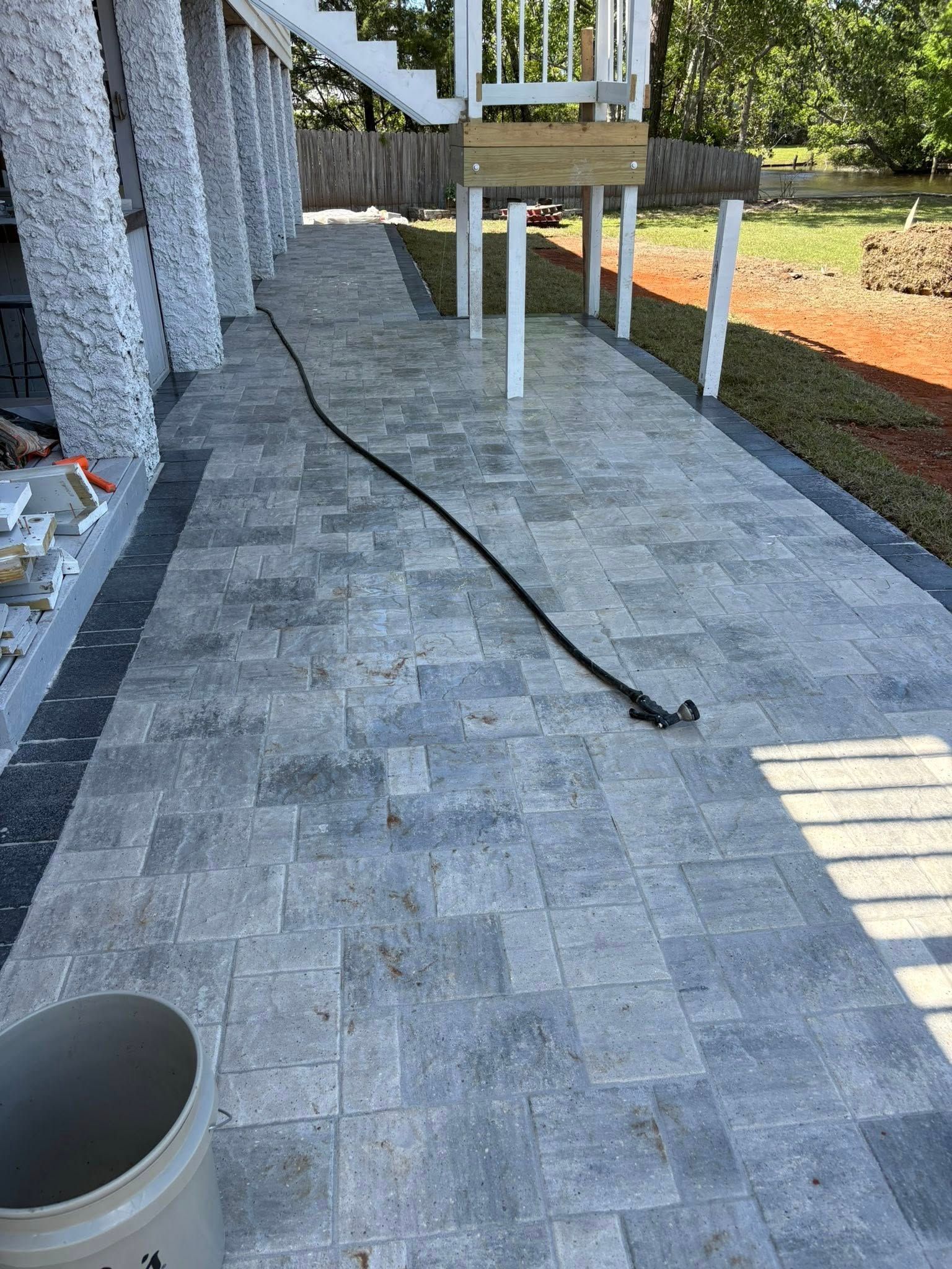 A walkway made of light gray stone pavers with a dark gray border, situated beneath an elevated deck with white supports.