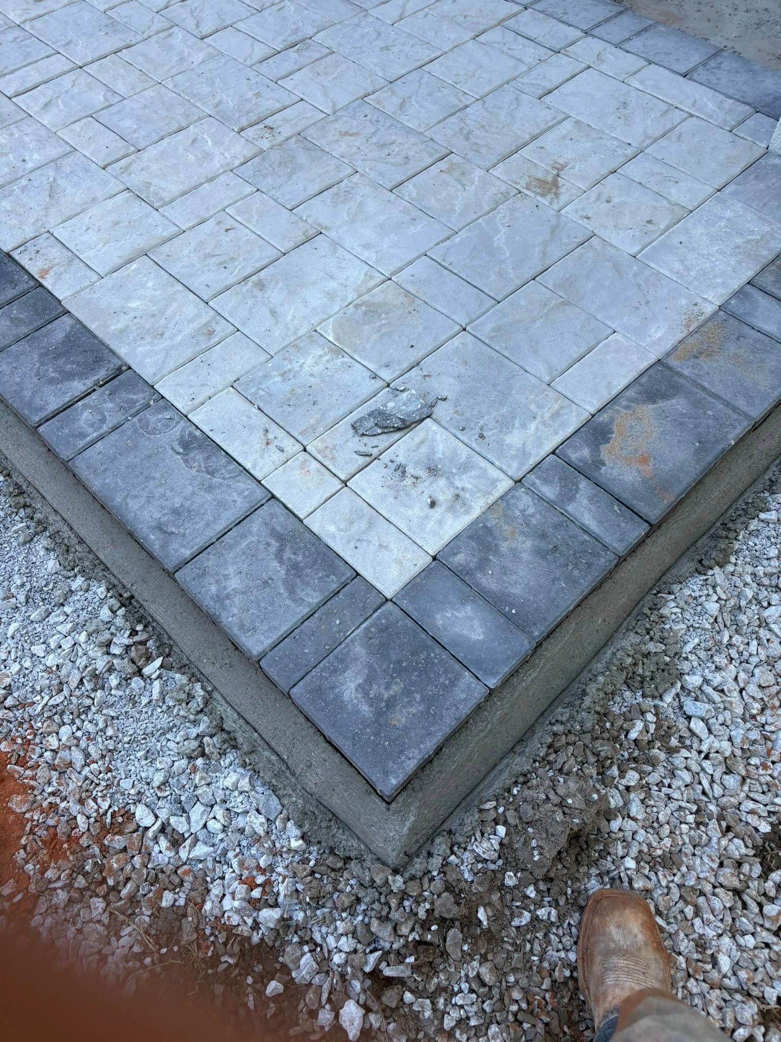 A corner of a newly laid patio featuring a light grey paver center bordered by dark grey stones set in concrete.