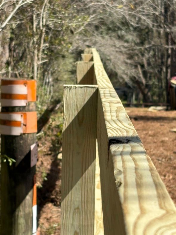 A close-up, angled view looking along the top edge of a newly installed wooden fence, beside a striped utility post.
