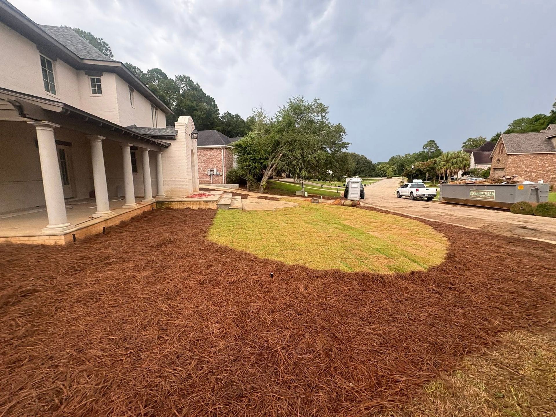 A house with a wraparound porch overlooking a front yard featuring a freshly shaped patch of grass surrounded by mulch.