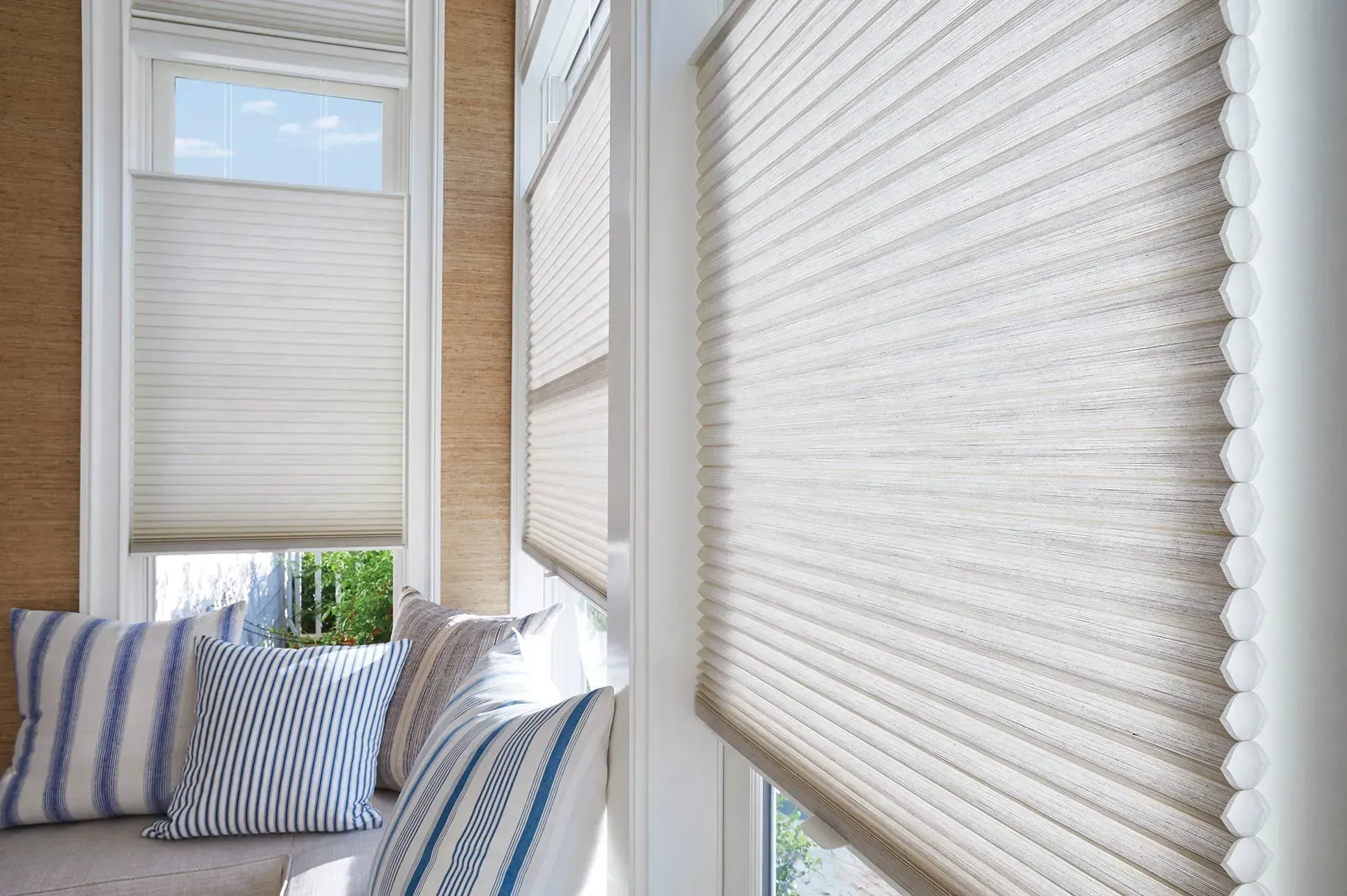 Window with light beige cellular shades, window seat, and striped pillows.