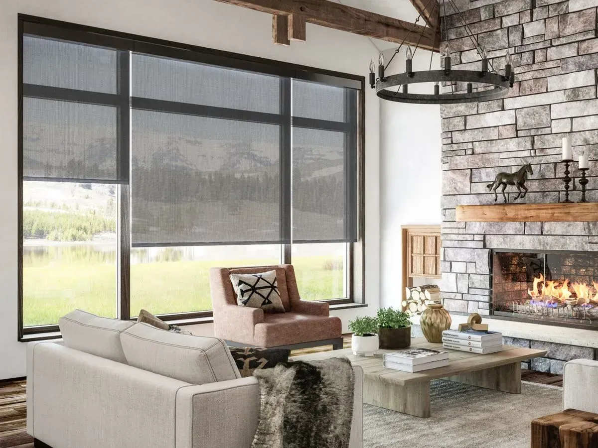 Living room with large windows, dark shades, stone fireplace, and rustic decor.