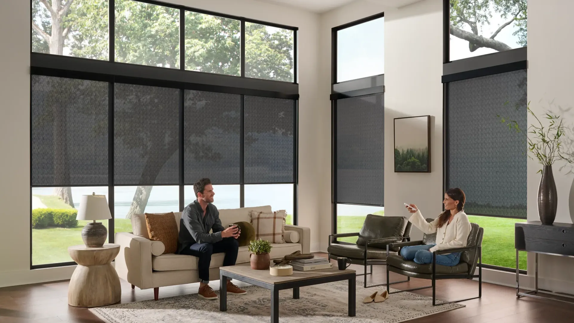 Living room with two people near windows with dark shades. A woman uses a remote.