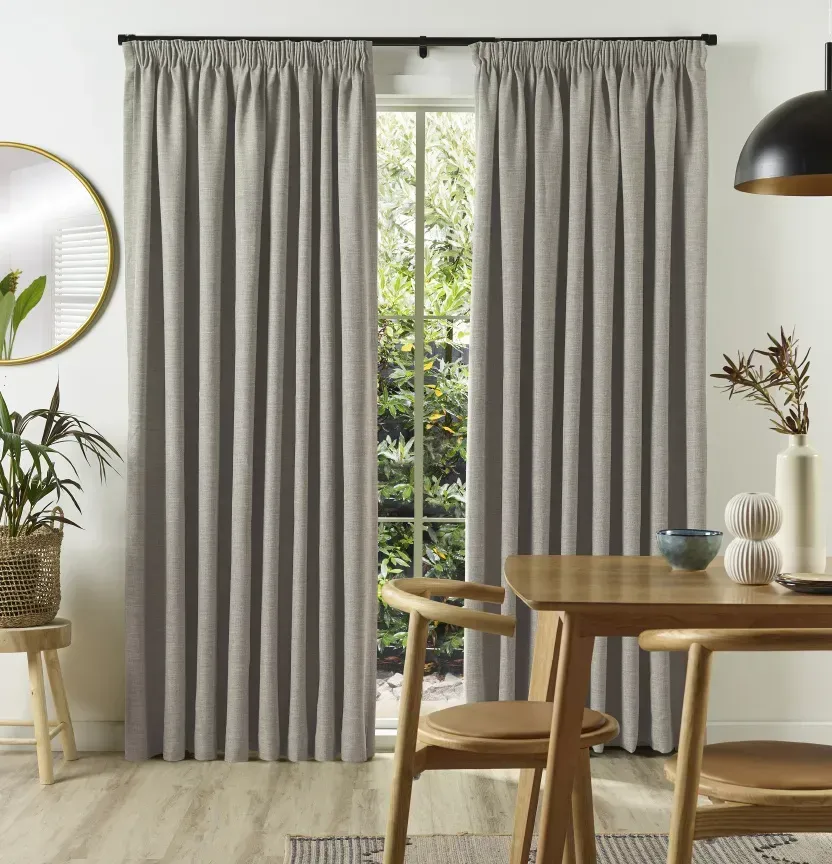 Dining room with neutral curtains framing a window, wooden table, chairs, mirror, and decorative items.