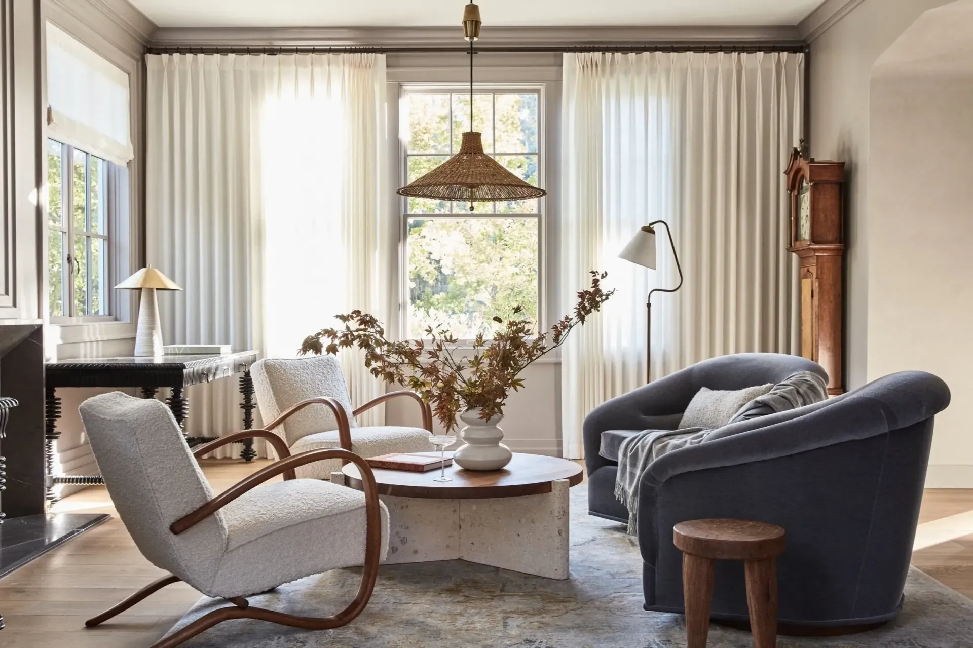 Cozy living room with neutral colors, two curved armchairs, a coffee table, and tall curtains.