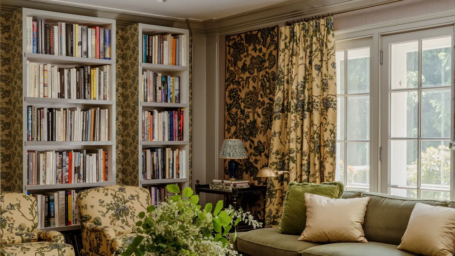 Living room with bookshelves, floral wallpaper, sofa, and curtains, green and beige color scheme.